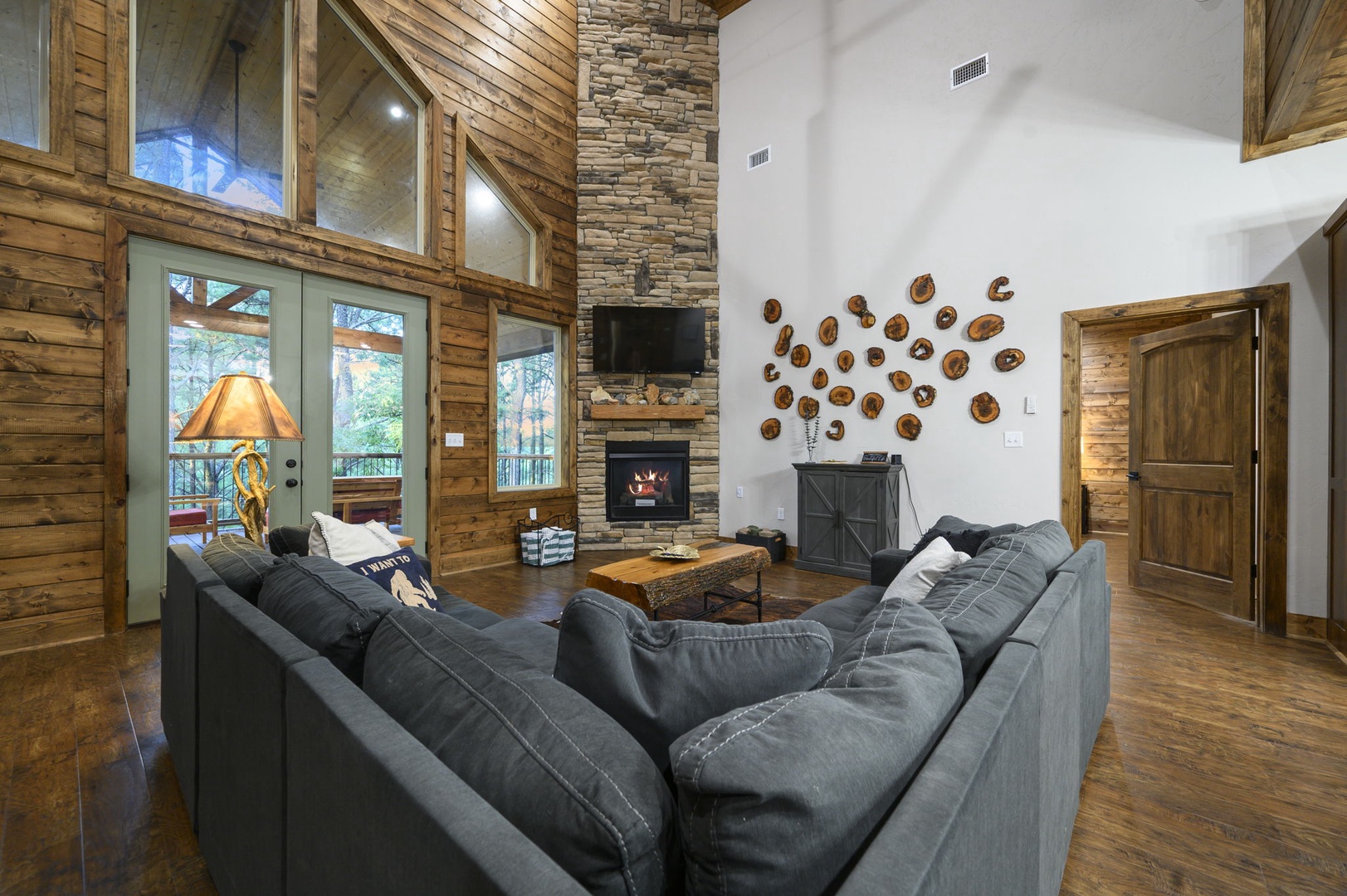 Sink into plush sectional seating beneath soaring vaulted ceilings, where warm wood tones and a stone fireplace create your perfect mountain retreat. Natural light pours through glass doors leading to your private deck with forest views.