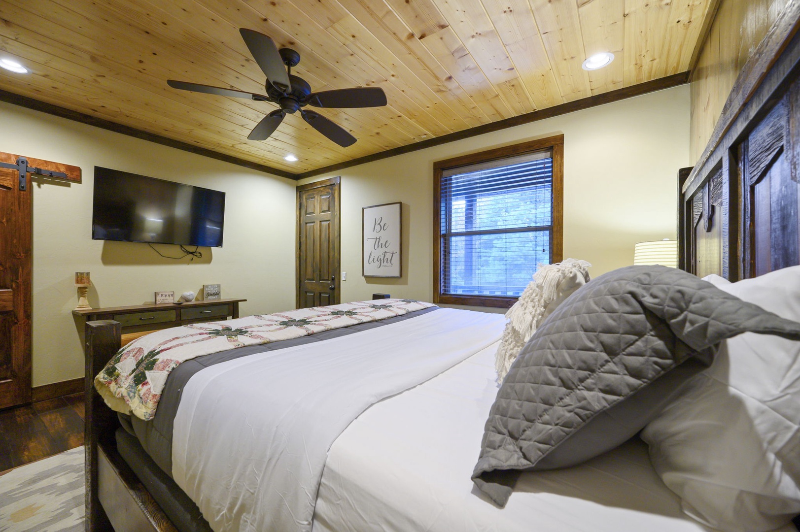 Unwind in your serene bedroom with a plush bed, charming wood-plank ceiling, and soft natural light filtering through. Rustic touches and thoughtful details create your perfect retreat.