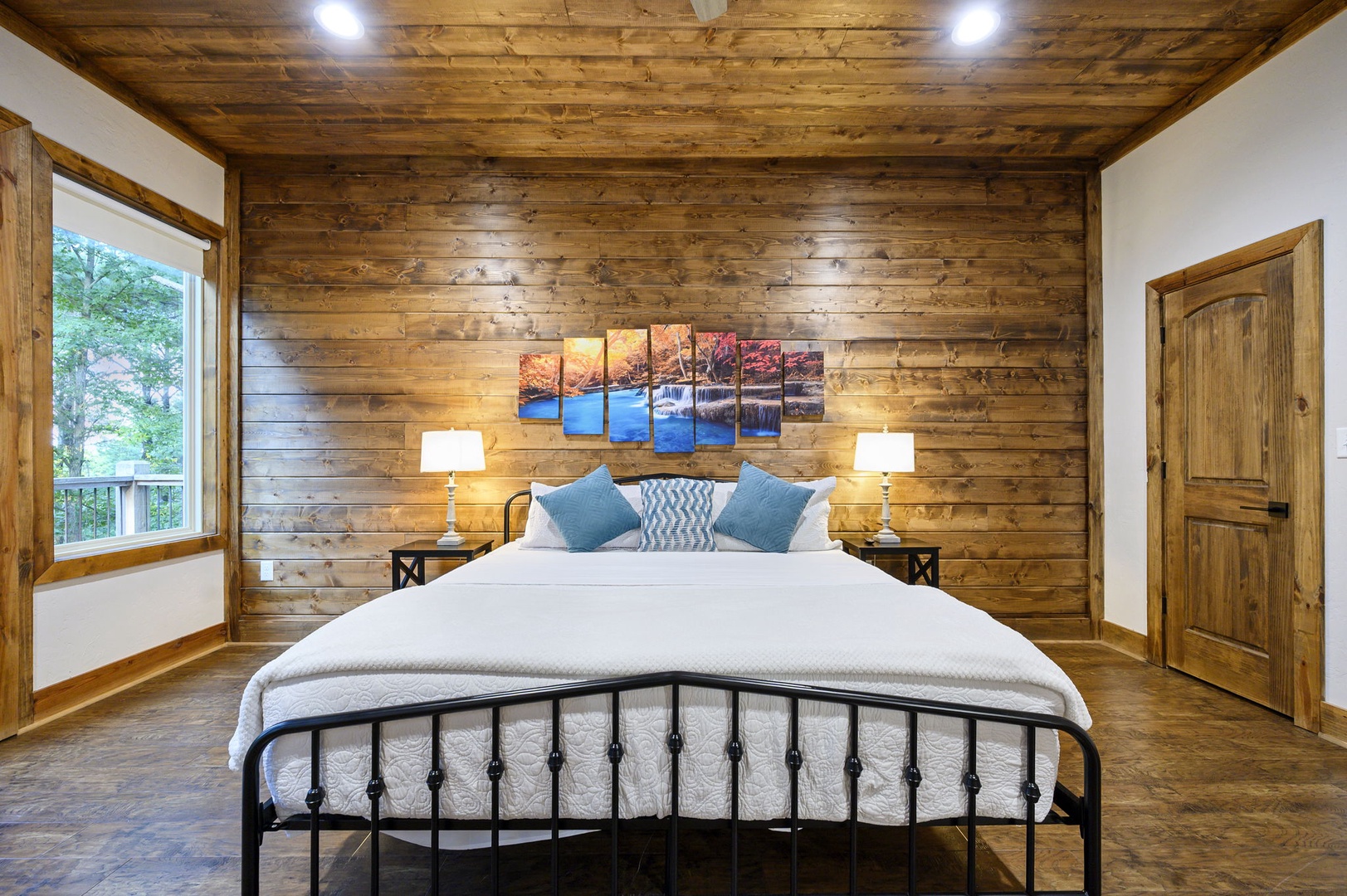 Unwind in your cozy retreat with rustic wood-paneled walls and a plush bed dressed in crisp linens. Natural light streams through the window, framing views of lush greenery and inviting you to relax completely.