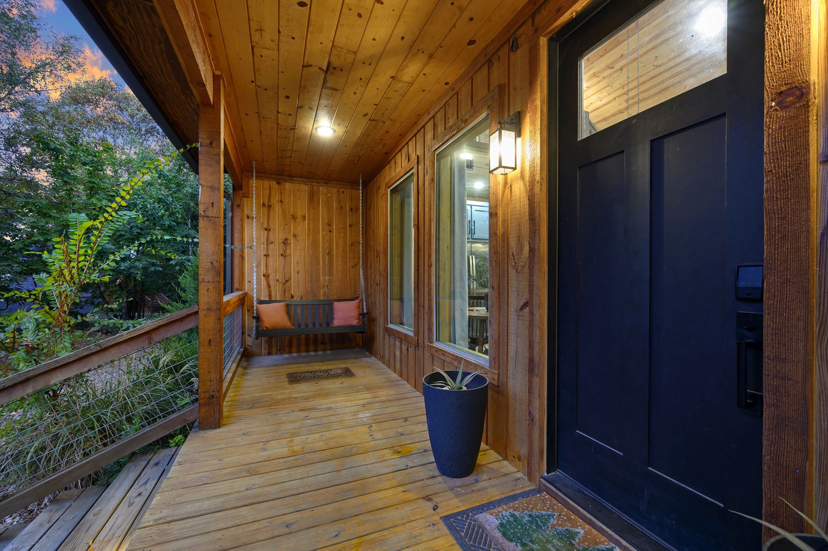 A welcoming covered entryway with warm wood finishes invites you home after a day of exploring, where a cozy bench awaits you to pause and savor the peaceful forest views.