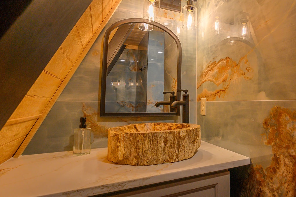 Refresh in your stunning bathroom featuring a rustic stone vessel sink, warm wood accents, and artistic marble walls that create a spa-like retreat perfect for unwinding after your adventures.