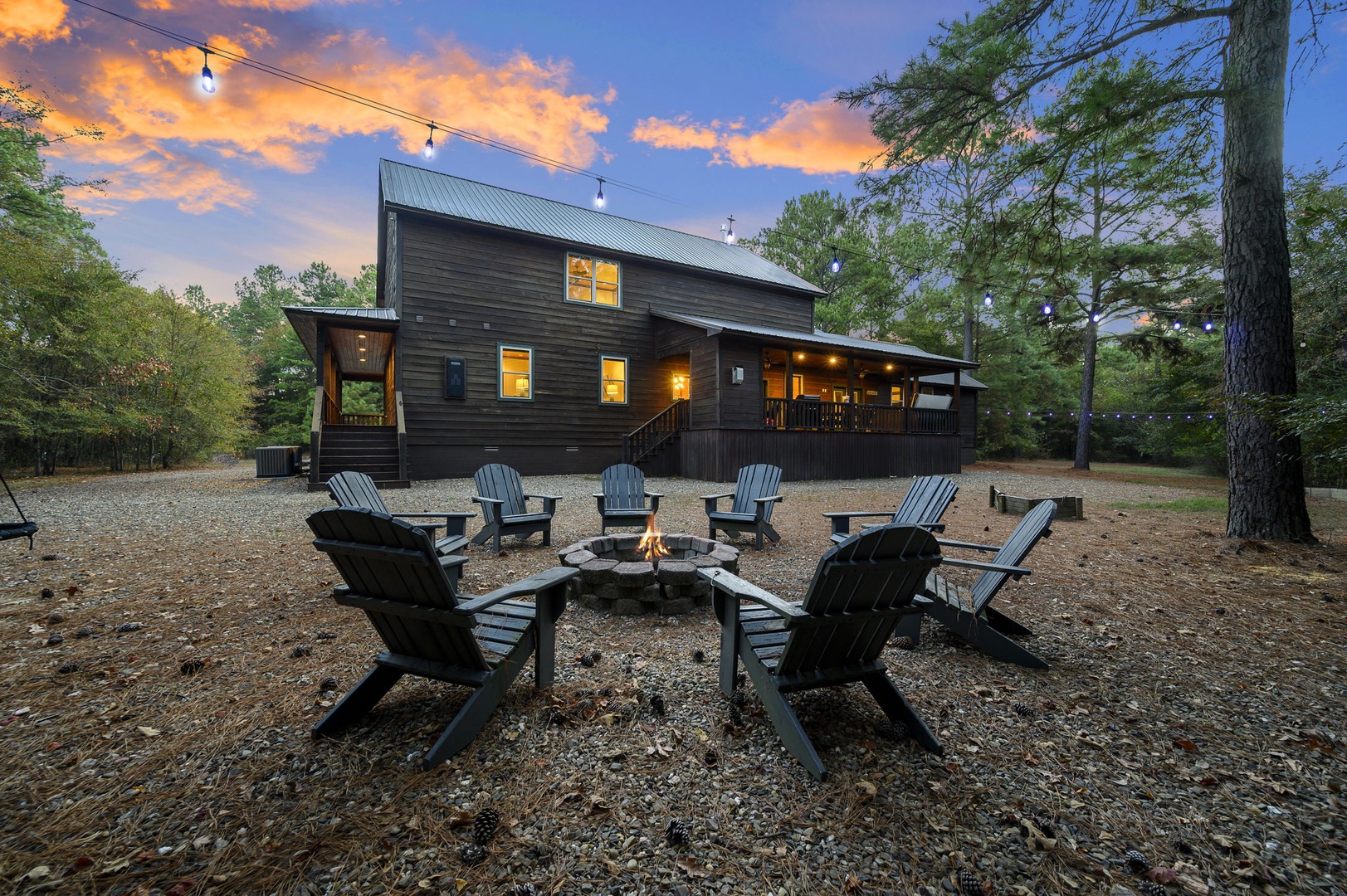 A tranquil evening retreat nestled among tall pines, where string lights glow softly overhead and Adirondack chairs circle a fire pit—perfect for stargazing or sharing stories under the sky.