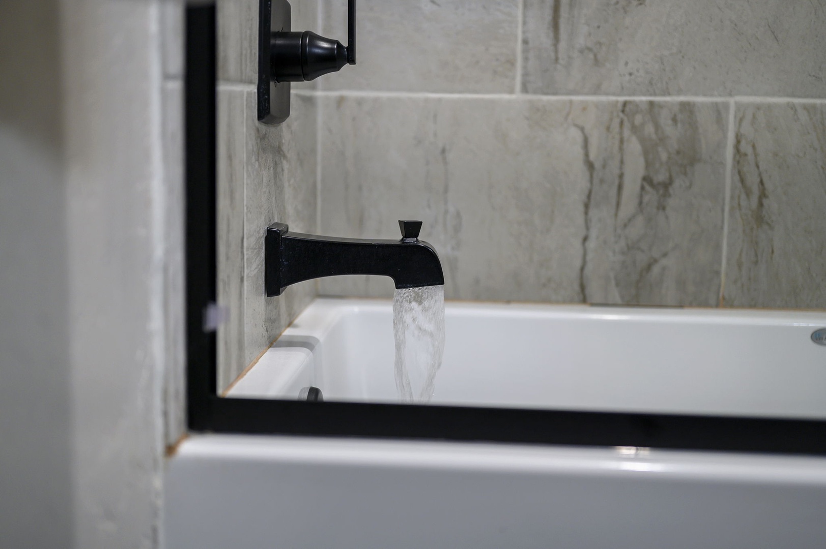 Soak in luxury. Your private bath features elegant marble-look tile and modern black fixtures, creating a sophisticated retreat for ultimate relaxation.