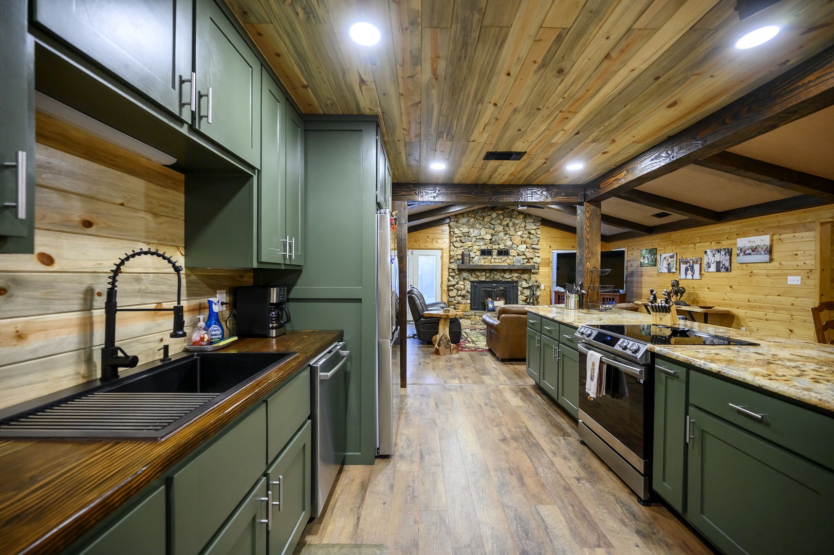 Your rustic chef's dream features sage green cabinets, granite countertops, and exposed beam ceilings that perfectly frame the cozy stone fireplace beyond. Please note that the fireplace is not available for guest use.
