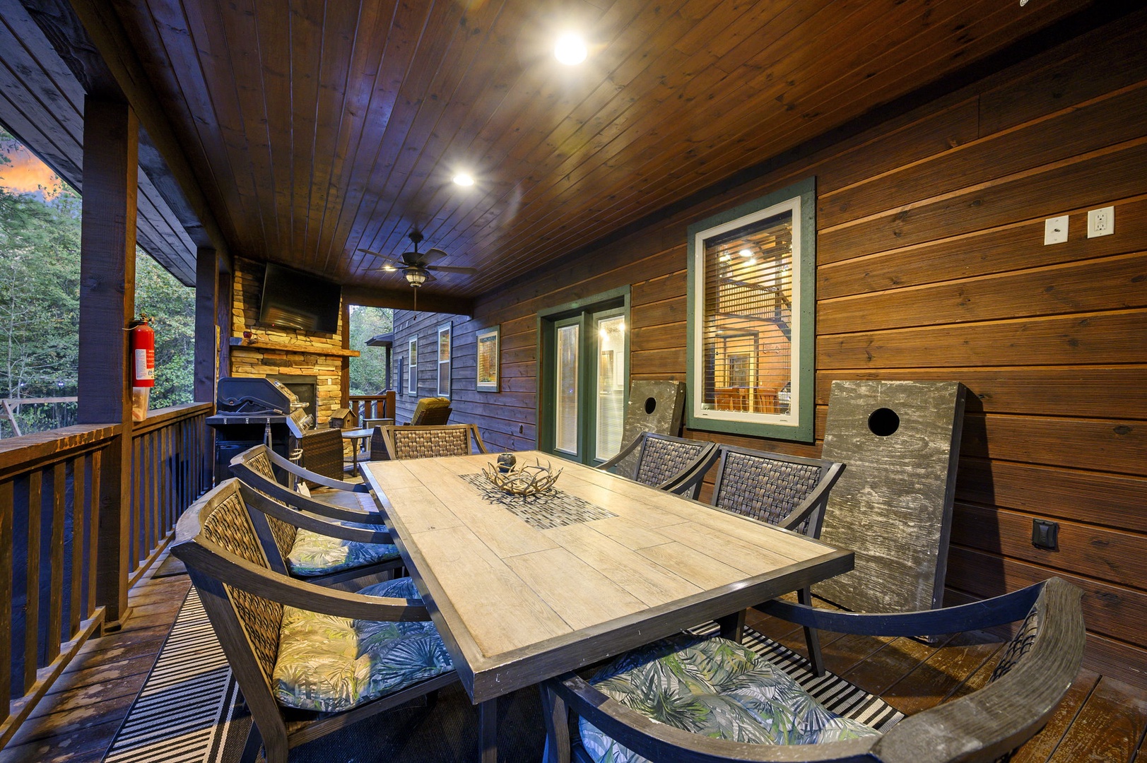 Gather around your private covered deck, where warm wood tones and soft lighting create the perfect setting for memorable meals and conversations under the ceiling fan's gentle breeze.