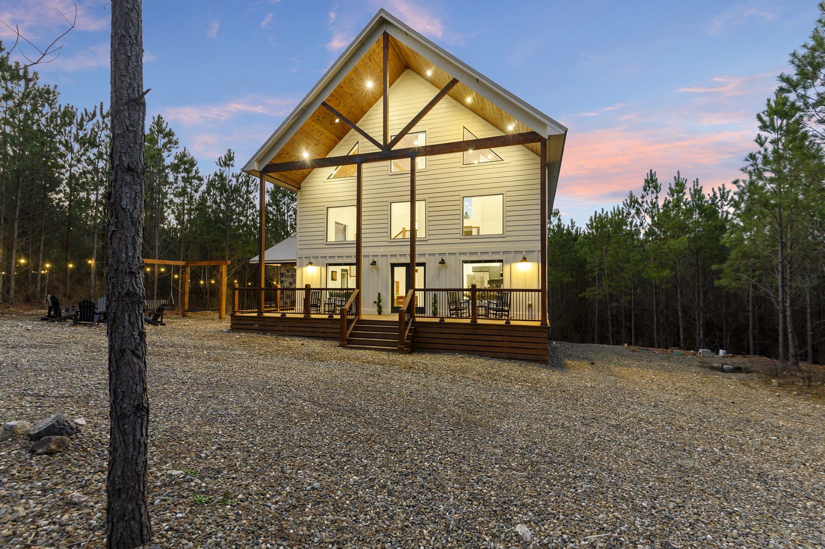 Modern cabin nestled in peaceful forest setting with expansive deck and dramatic lighting against twilight sky.
