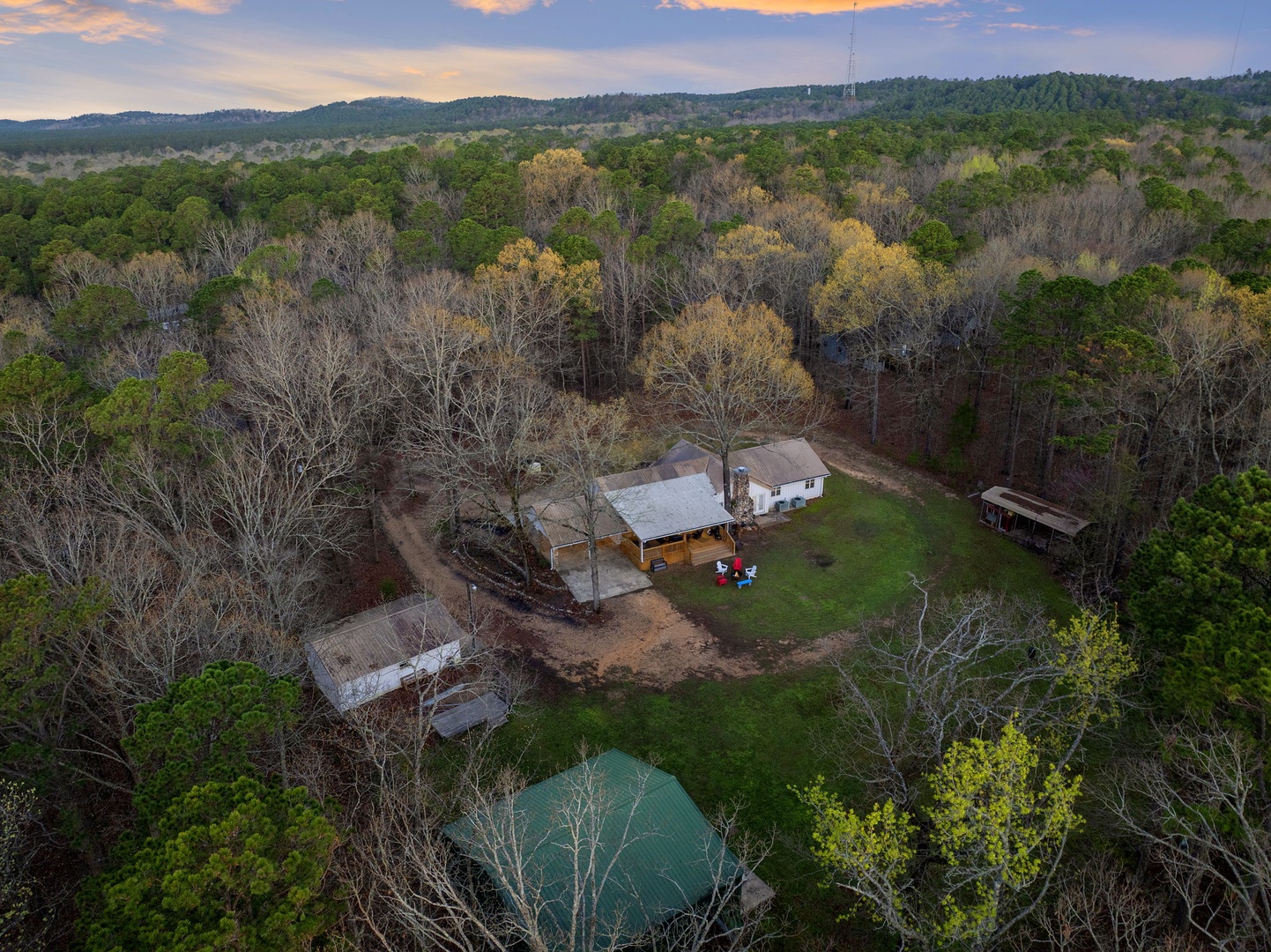 Secluded farmhouse property nestled among rolling hills and forest, featuring rustic buildings and peaceful rural surroundings.
