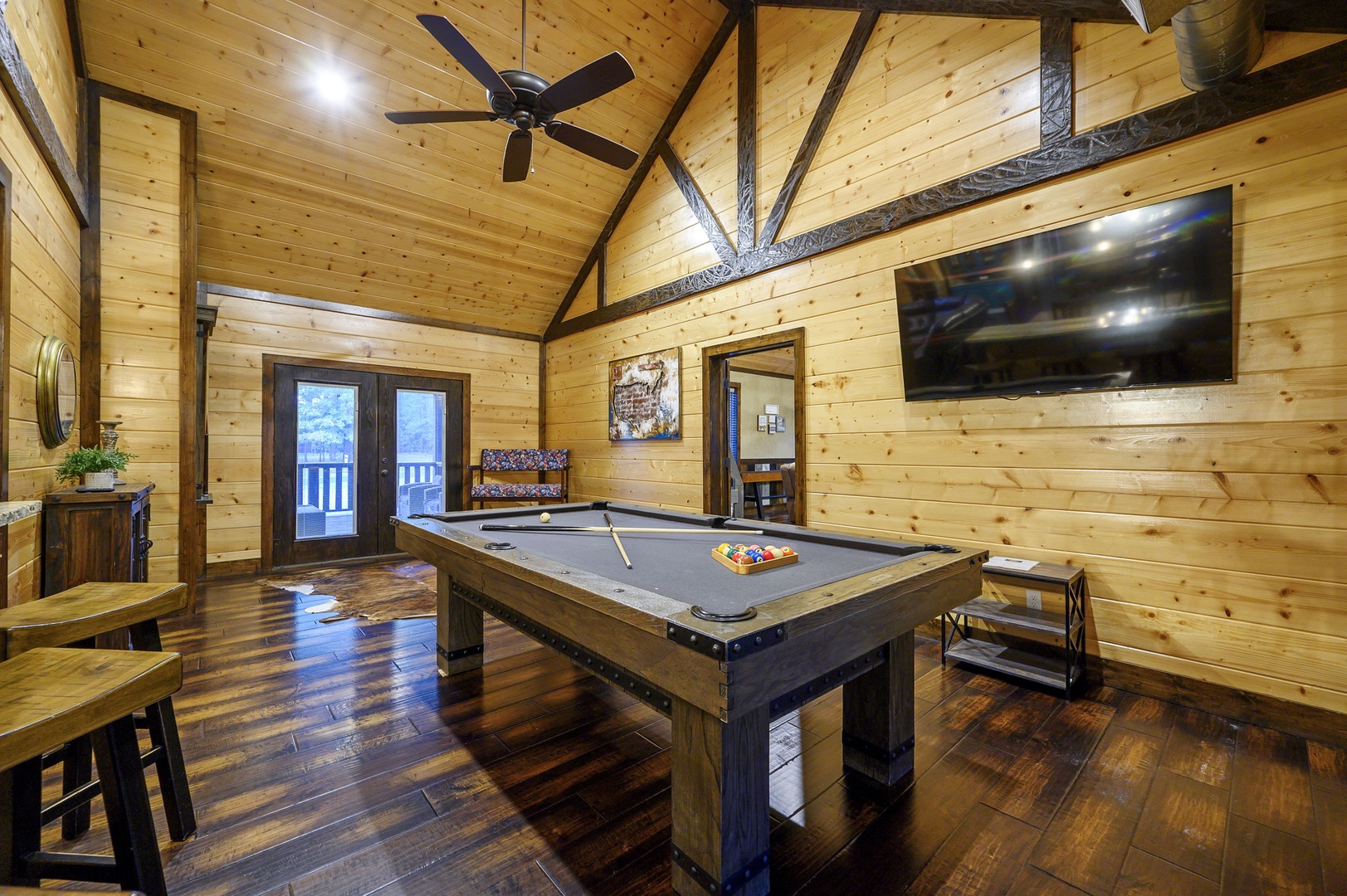 Step into your private game room with vaulted ceilings, exposed beams, and rich wood floors—perfect for pool tournaments or cozy downtime beneath the gentle hum of the ceiling fan.