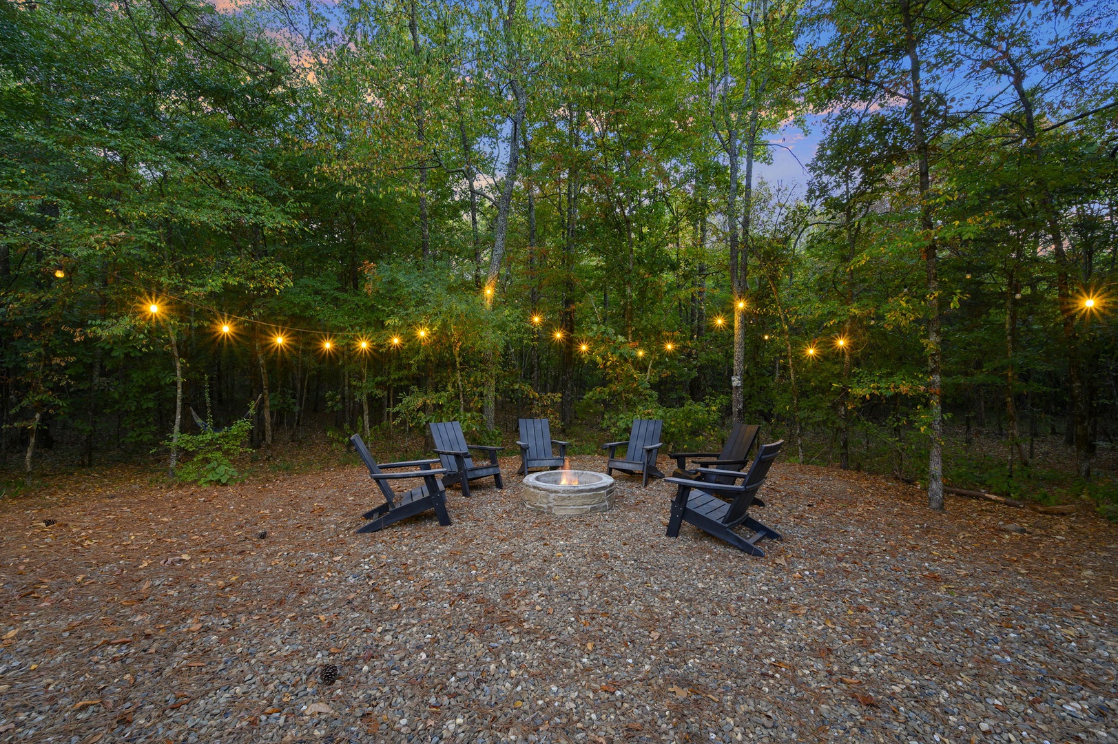 A private fire pit nestled in the woods awaits your evenings under the string lights, where the crackling flames and forest air make every night feel like a peaceful escape.