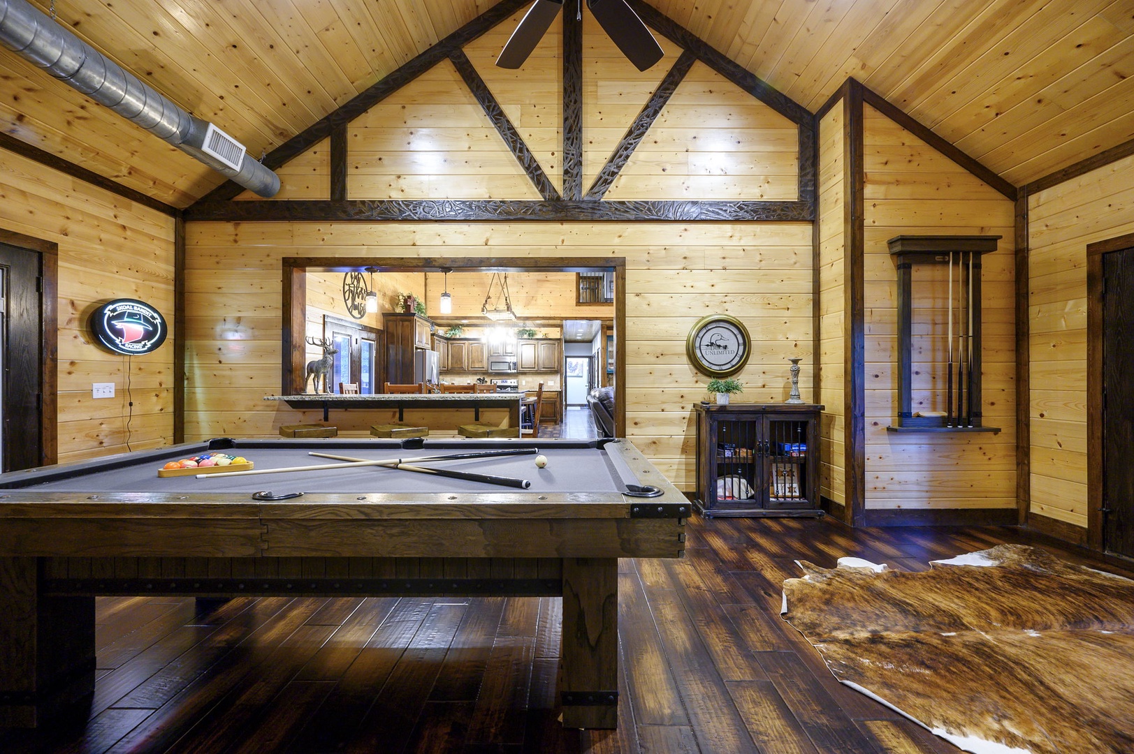 Step into your own rustic game room, where soaring wood-beam ceilings and a pool table invite friendly competition under warm lighting, with the kitchen just beyond ready for snacks and drinks.
