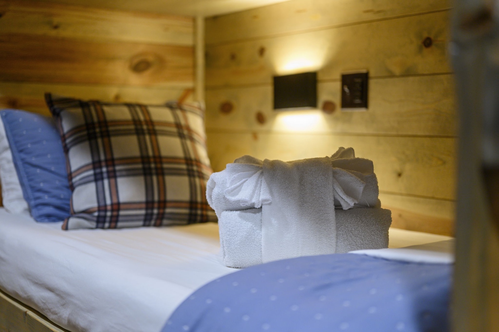 Cozy up in this charming bunk room with fresh linens and towels waiting just for you. The warm wood paneling and soft lighting create a relaxing cabin feel.