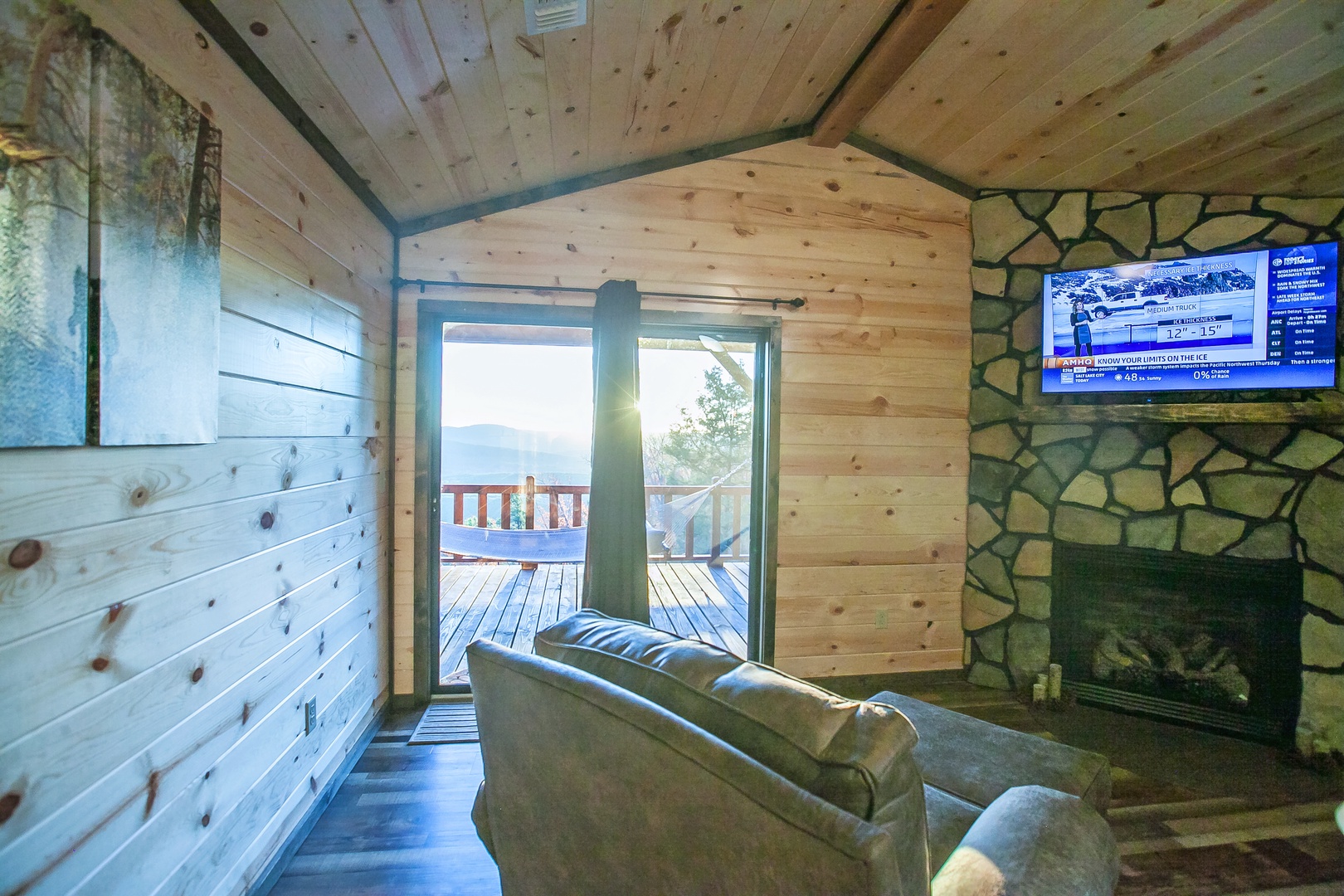 Your cozy living room features rustic wood walls and stone fireplace, with mountain views through sliding doors to your private deck.