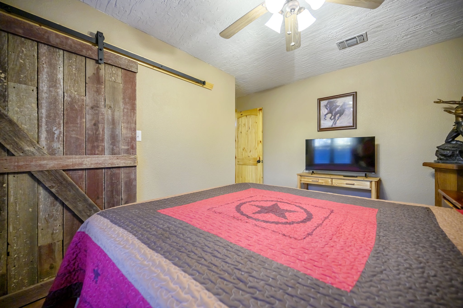 Unwind in your rustic bedroom featuring a unique barn door, cozy Western decor, and modern TV for your evening entertainment.