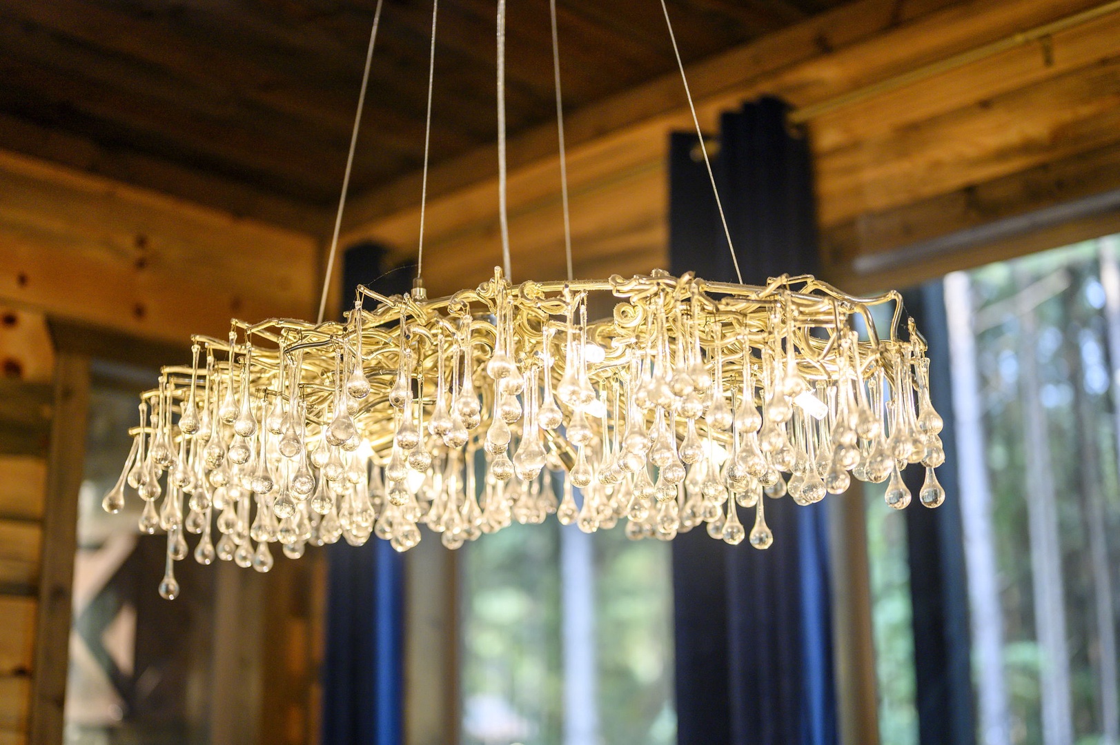 A stunning crystal chandelier illuminates the space with warm, sparkling light, complementing the natural wood ceiling and creating an elegant, inviting atmosphere.
