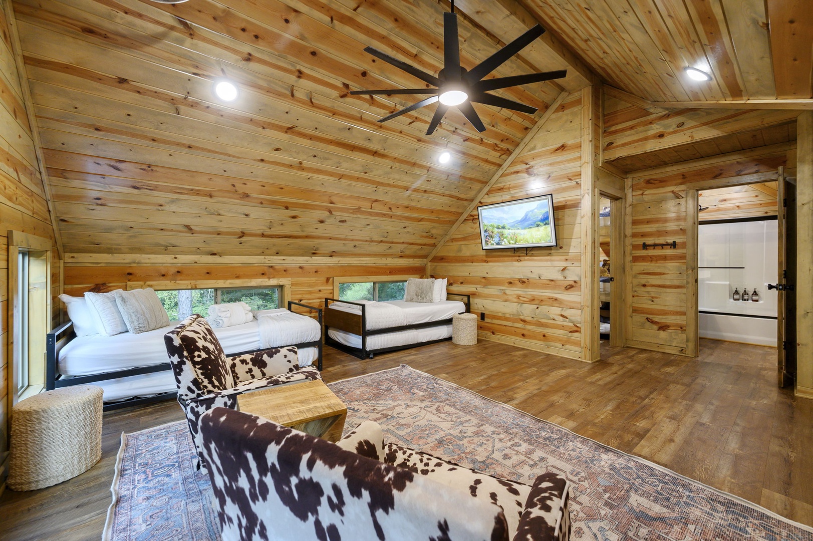 Warm wood-planked walls and vaulted ceilings create a cozy retreat where you can unwind in rustic comfort. Two plush daybeds and a soft accent chair invite you to relax beneath soft lighting and modern style.