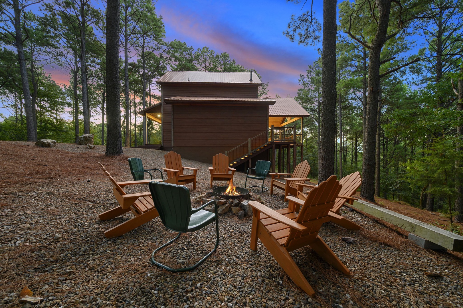 A charming cabin retreat nestled among towering pines, featuring a welcoming fire pit surrounded by Adirondack chairs—perfect for gathering under vibrant evening skies.