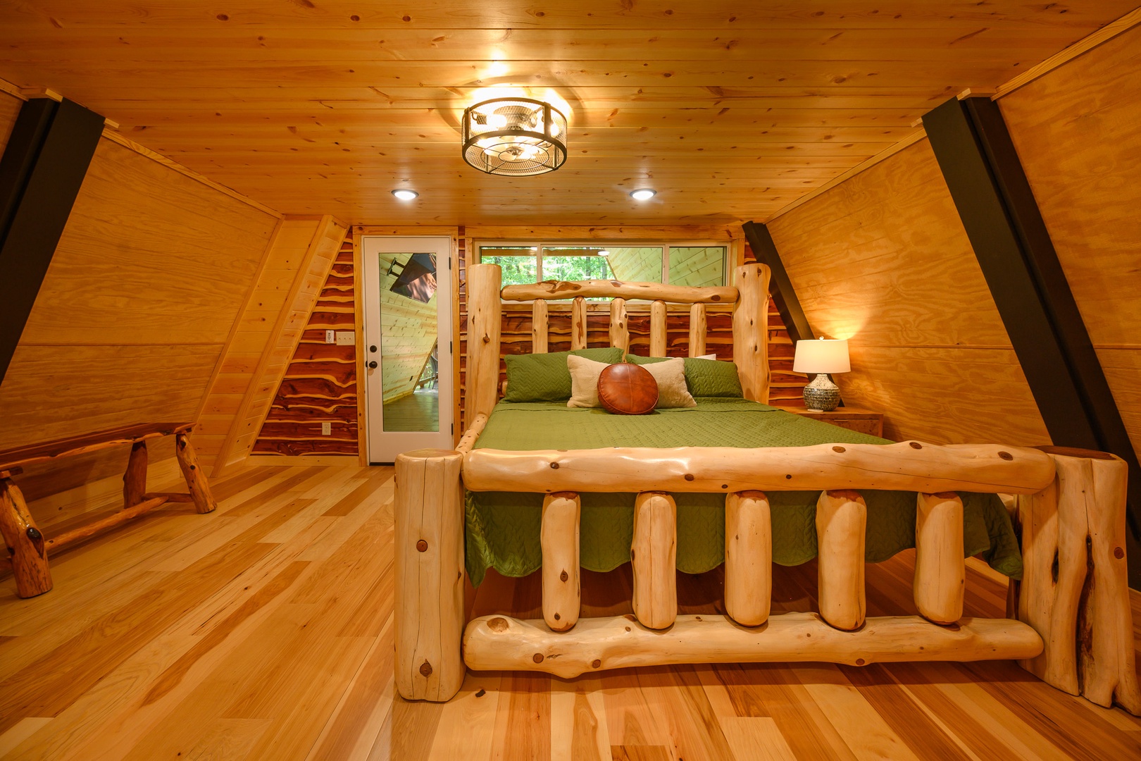 Unwind in your cozy loft bedroom, where handcrafted log furnishings and warm wood surround you. Natural light filters through the window, inviting peaceful forest views into your private retreat.