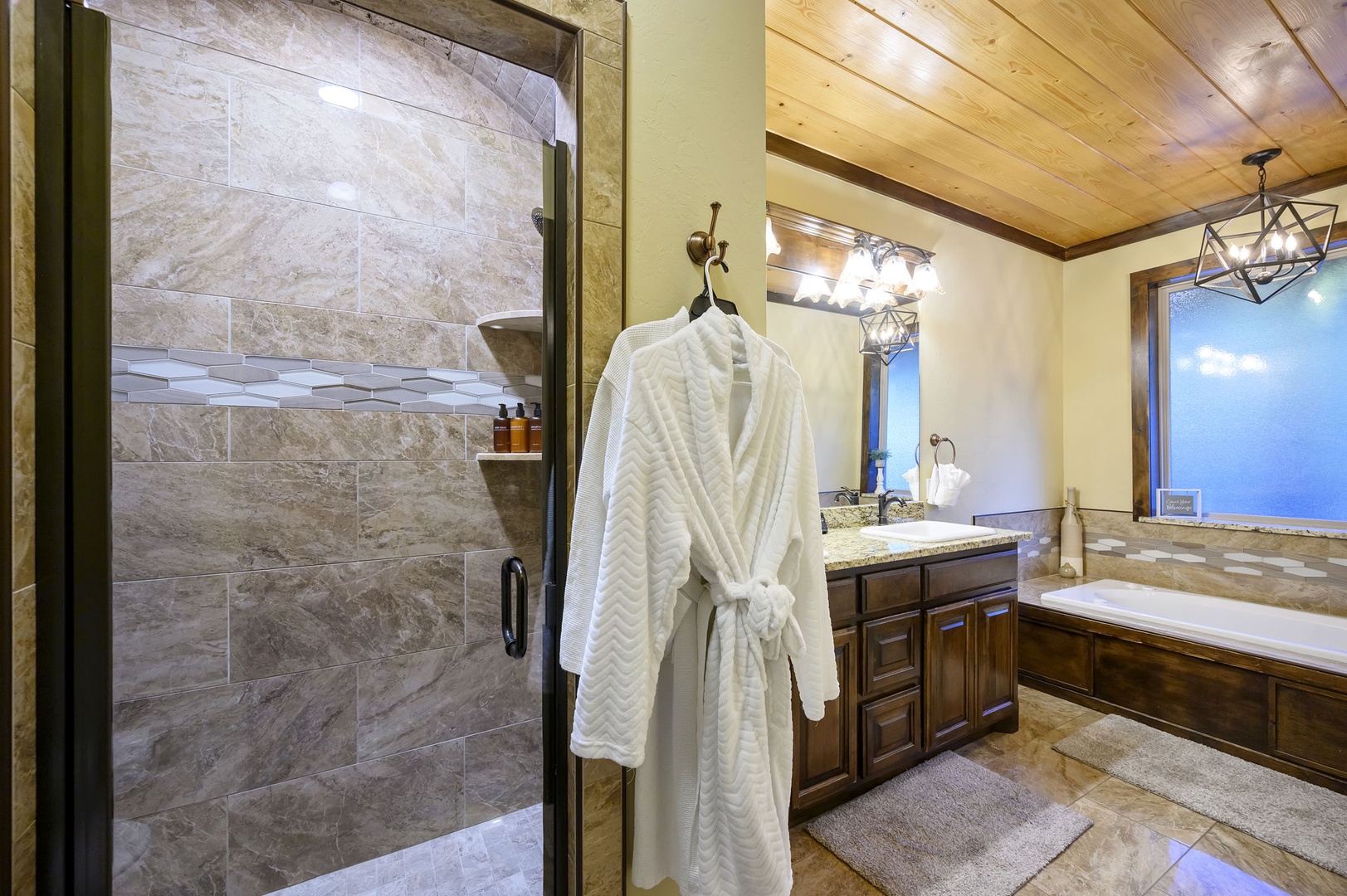 Step into your spa-like bathroom with elegant stone finishes, a spacious walk-in shower, and a plush robe waiting just for you—luxury meets mountain comfort.
