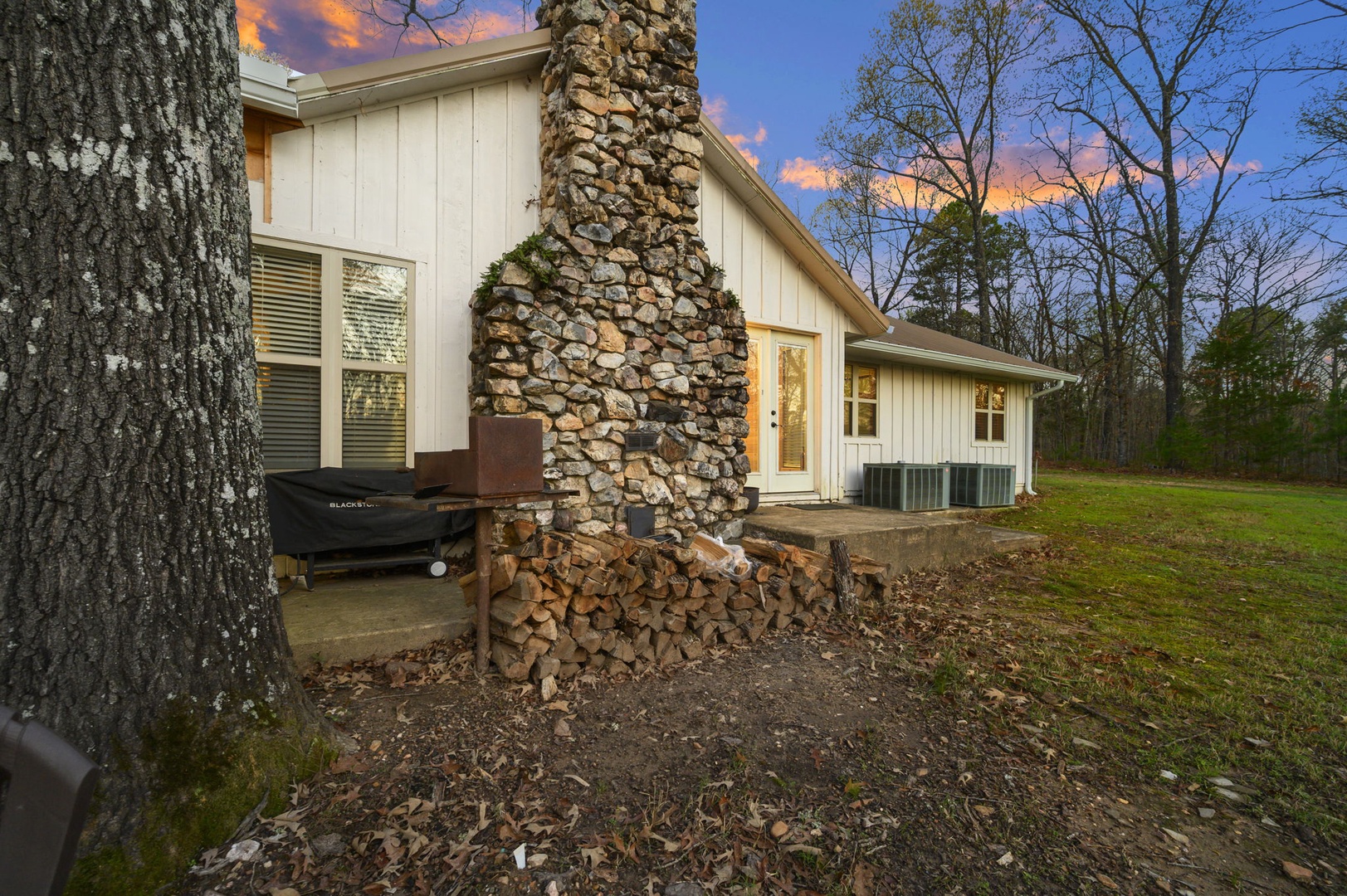 Modern farmhouse with striking stone chimney sits peacefully among towering trees, offering a serene countryside retreat. Please note that the fireplace is not available for guest use.