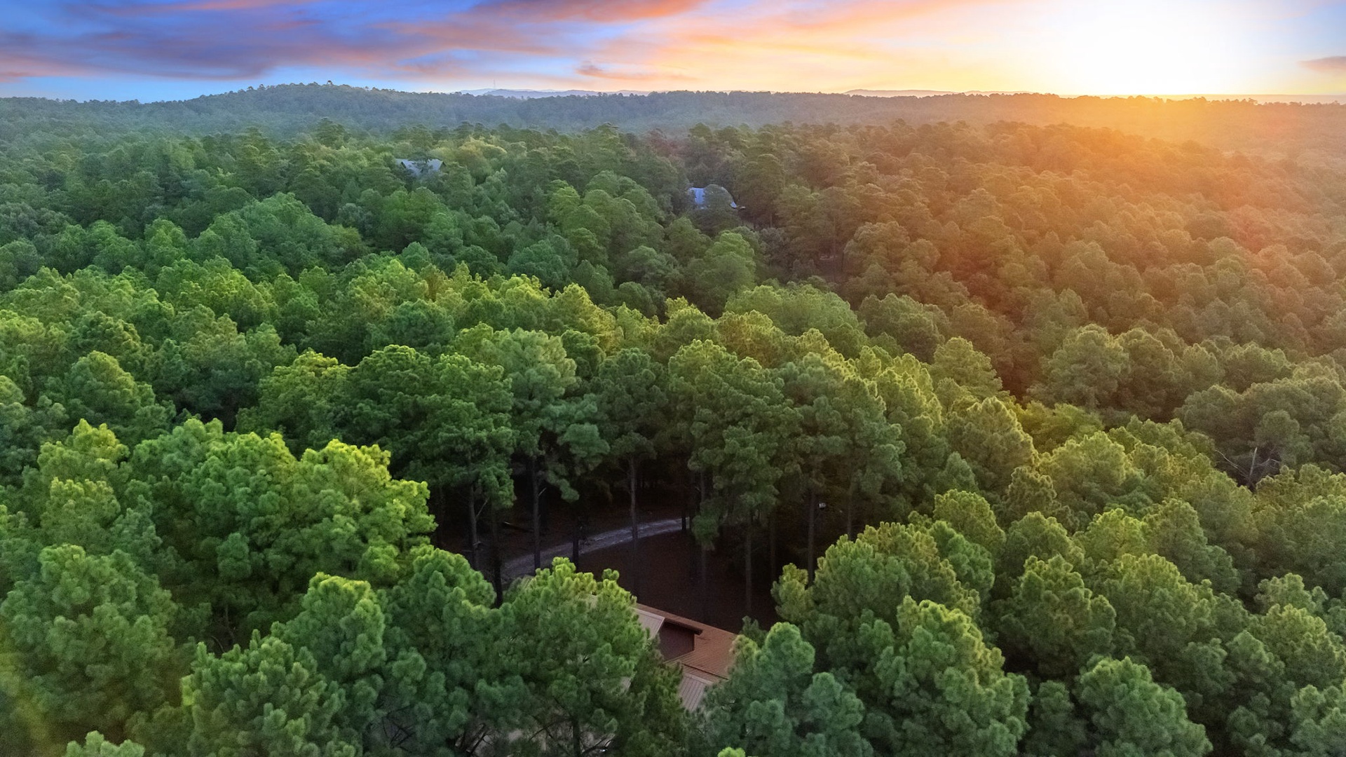 Aerial view of the property nestled among lush forested hills, bathed in the warm glow of sunset, offering a secluded natural retreat.