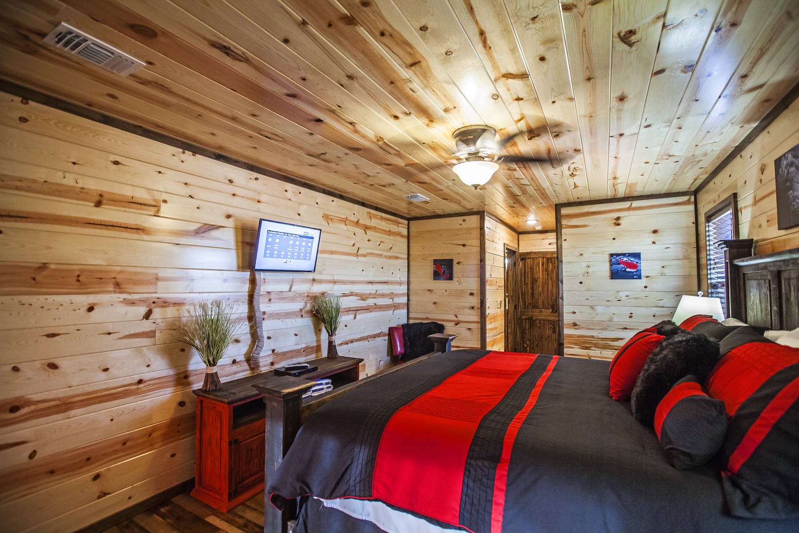Unwind in your cozy cabin bedroom with rustic wood beams, a wall-mounted TV, and bold red accents for the perfect mountain retreat.