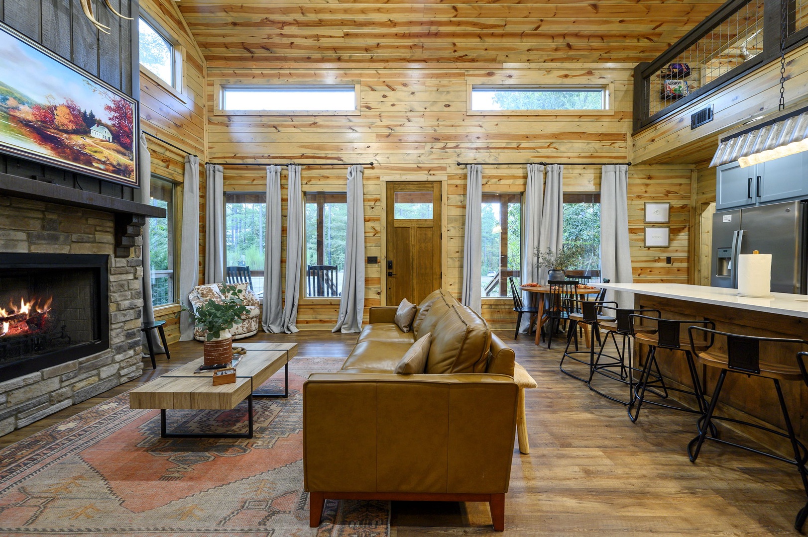 Relax in your inviting open-concept cabin, where warm wood surrounds you, a cozy fireplace crackles to life, and sunlight streams through expansive windows overlooking the tranquil natural landscape beyond.