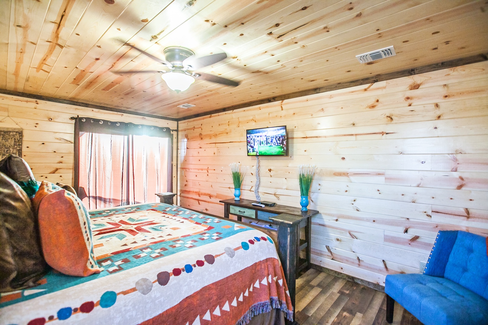 Cozy log cabin bedroom with rustic wood walls, colorful bedding, and your own TV for relaxing evenings in.