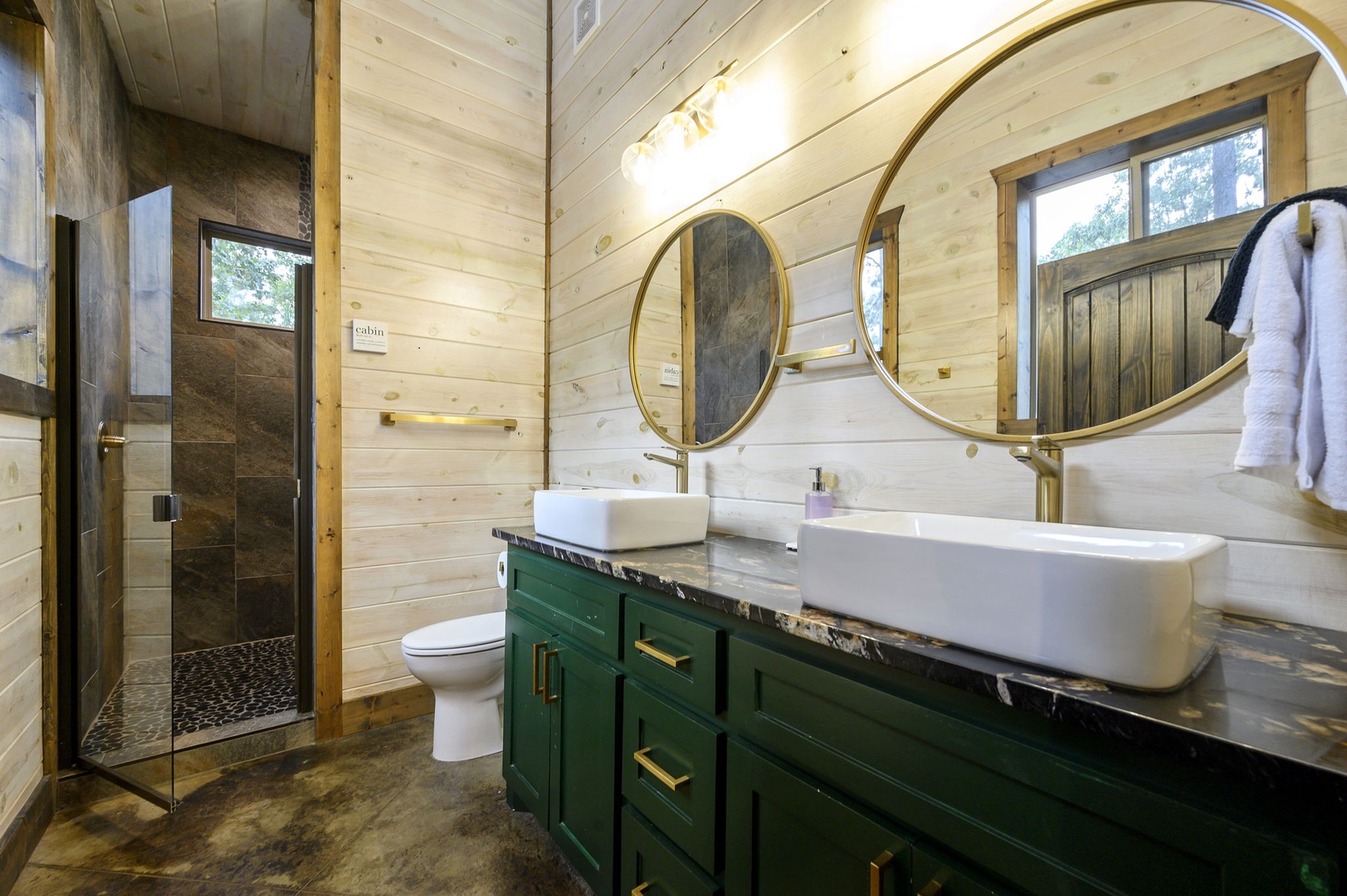 Step into your private spa-like retreat with dual vessel sinks, gleaming gold-framed mirrors, and a spacious walk-in shower—where modern elegance meets cozy cabin charm.