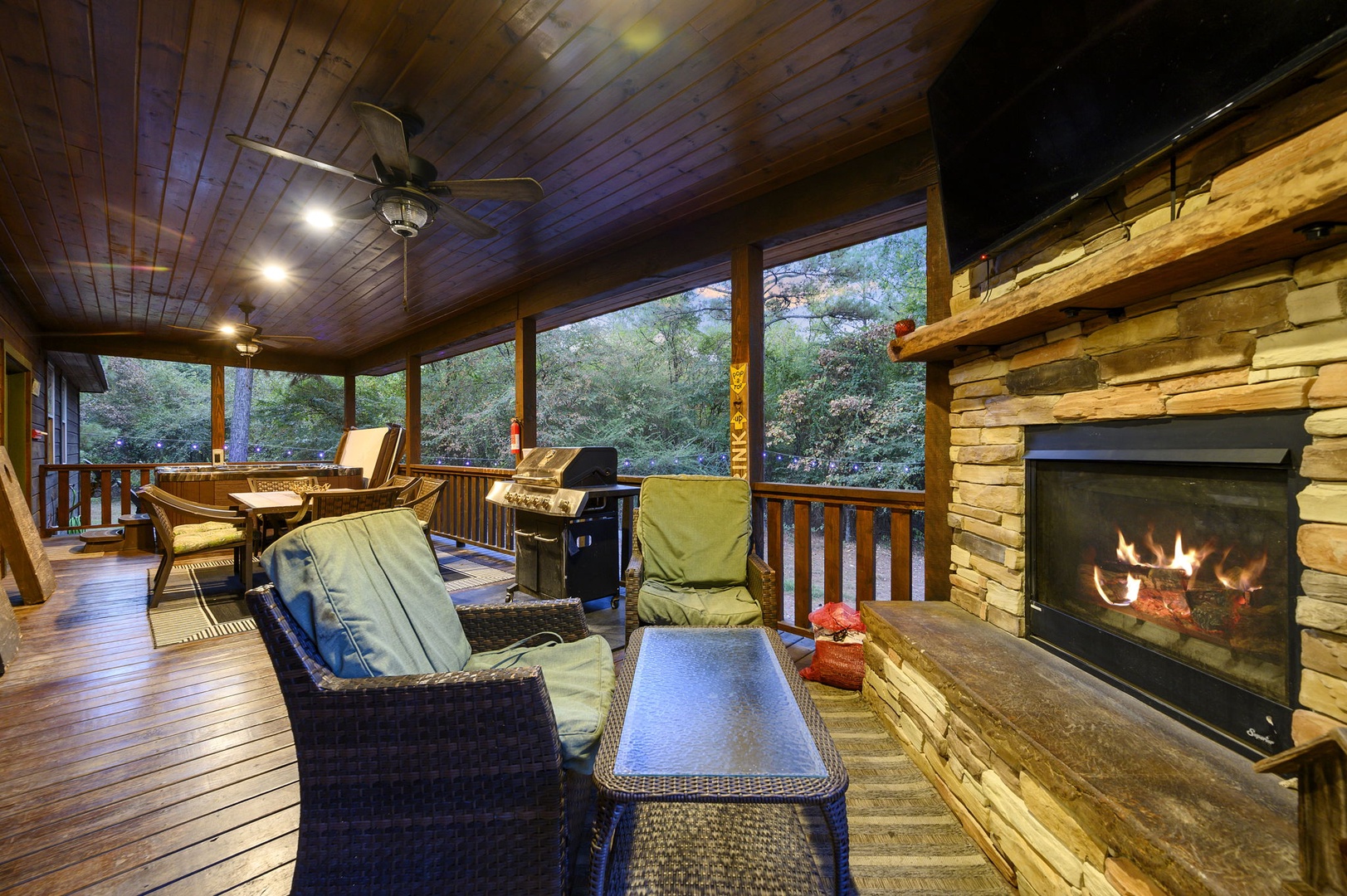 Curl up by the stone fireplace on this screened porch, where forest views and cozy seating create your perfect mountain retreat.