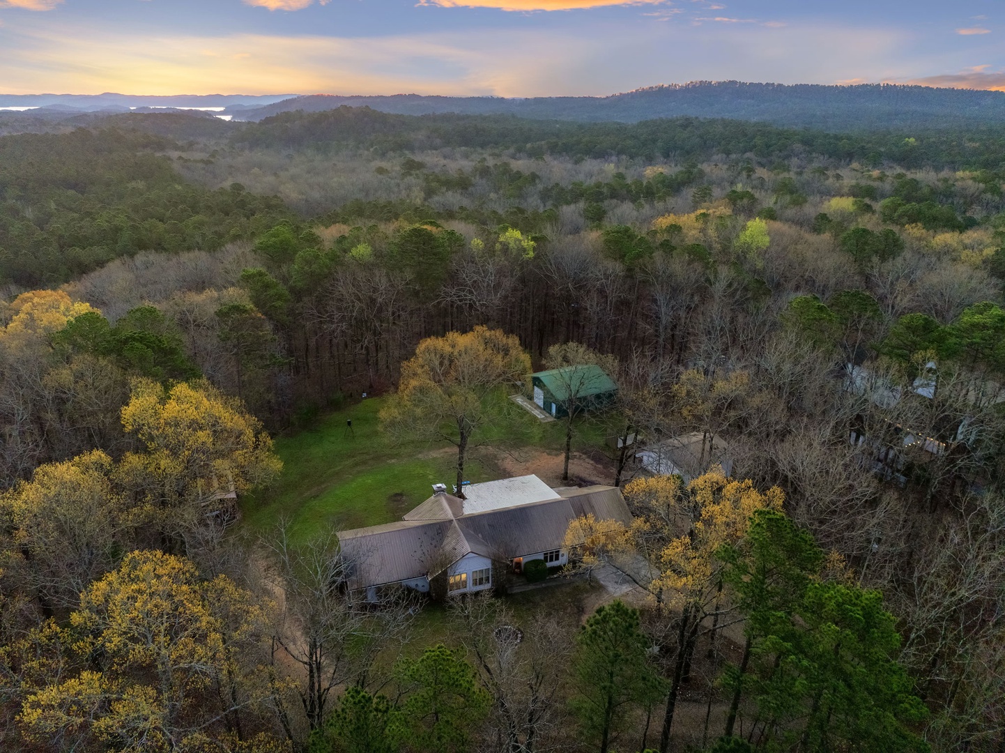 Secluded property nestled among rolling hills and spring foliage, offering peaceful countryside retreat with mountain backdrop at golden hour.
