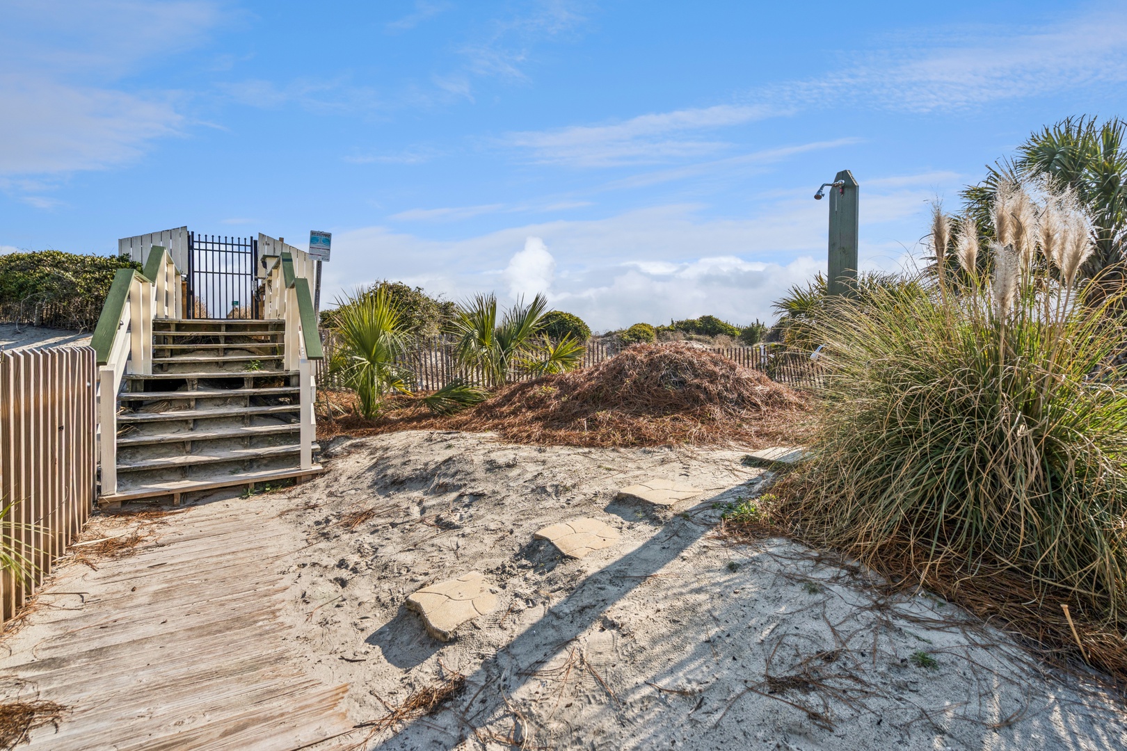 Beach access pathway features wooden stairs and tropical vegetation leading to sandy shores and coastal areas.