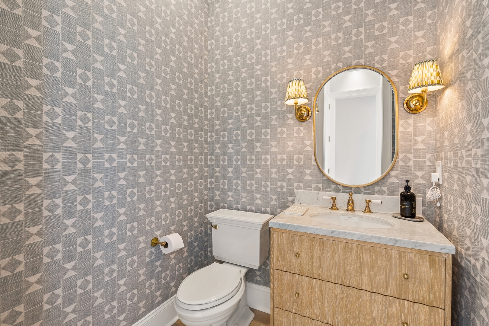Your bathroom features elegant geometric wallpaper, warm brass fixtures, and a sophisticated marble-topped vanity that creates a luxurious powder room experience.