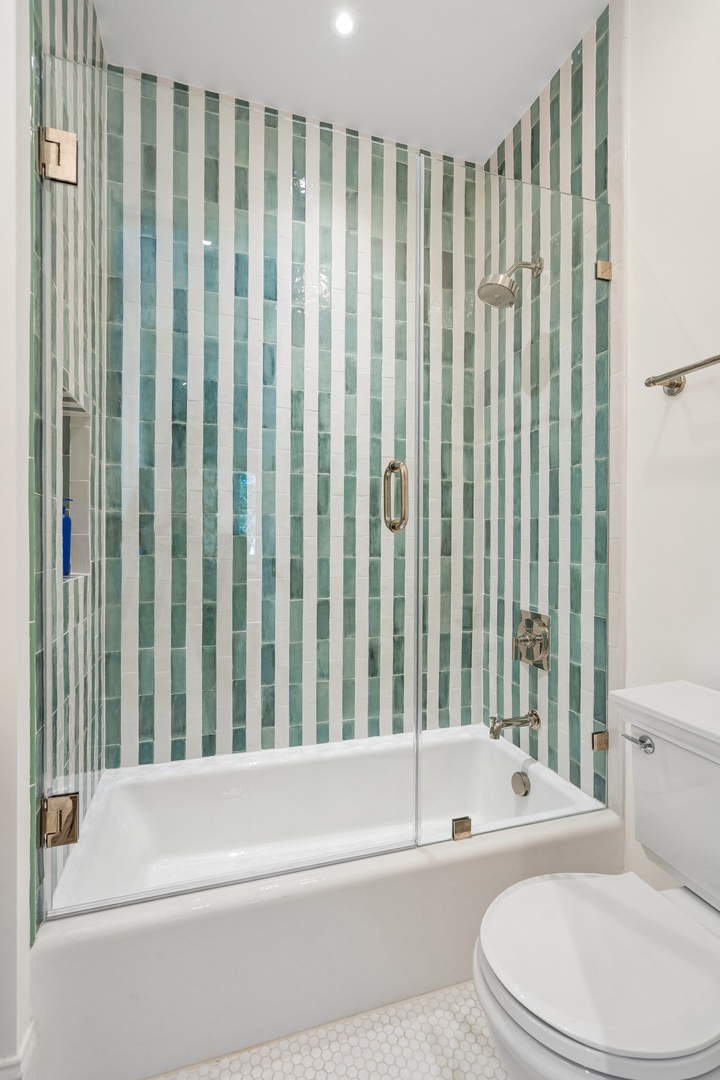 Step into your bright, spotless bathroom with cheerful green striped tile and a pristine tub-shower combo perfect for unwinding after a day of exploring.