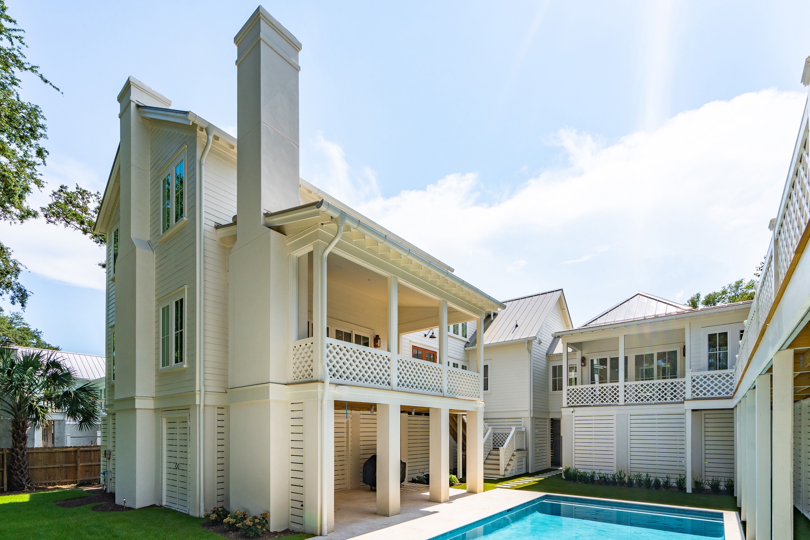 An elegant coastal-style property showcasing classic architecture with clean white siding, twin chimneys, and a private pool nestled in a lush, quiet neighborhood setting.