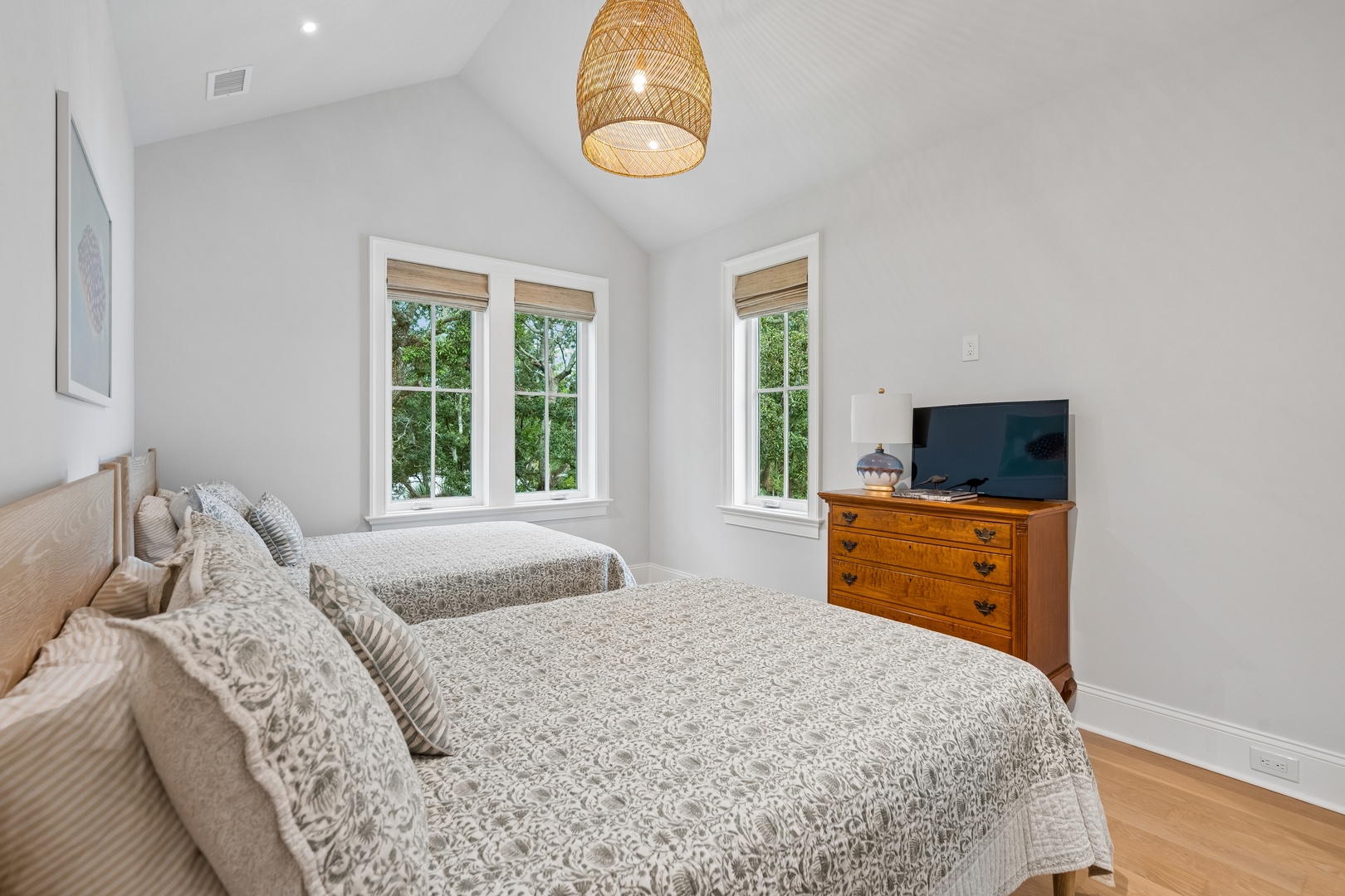 Rest easy in this serene twin bedroom where soft linens and a woven pendant light create your peaceful retreat, with garden views just beyond your windows.