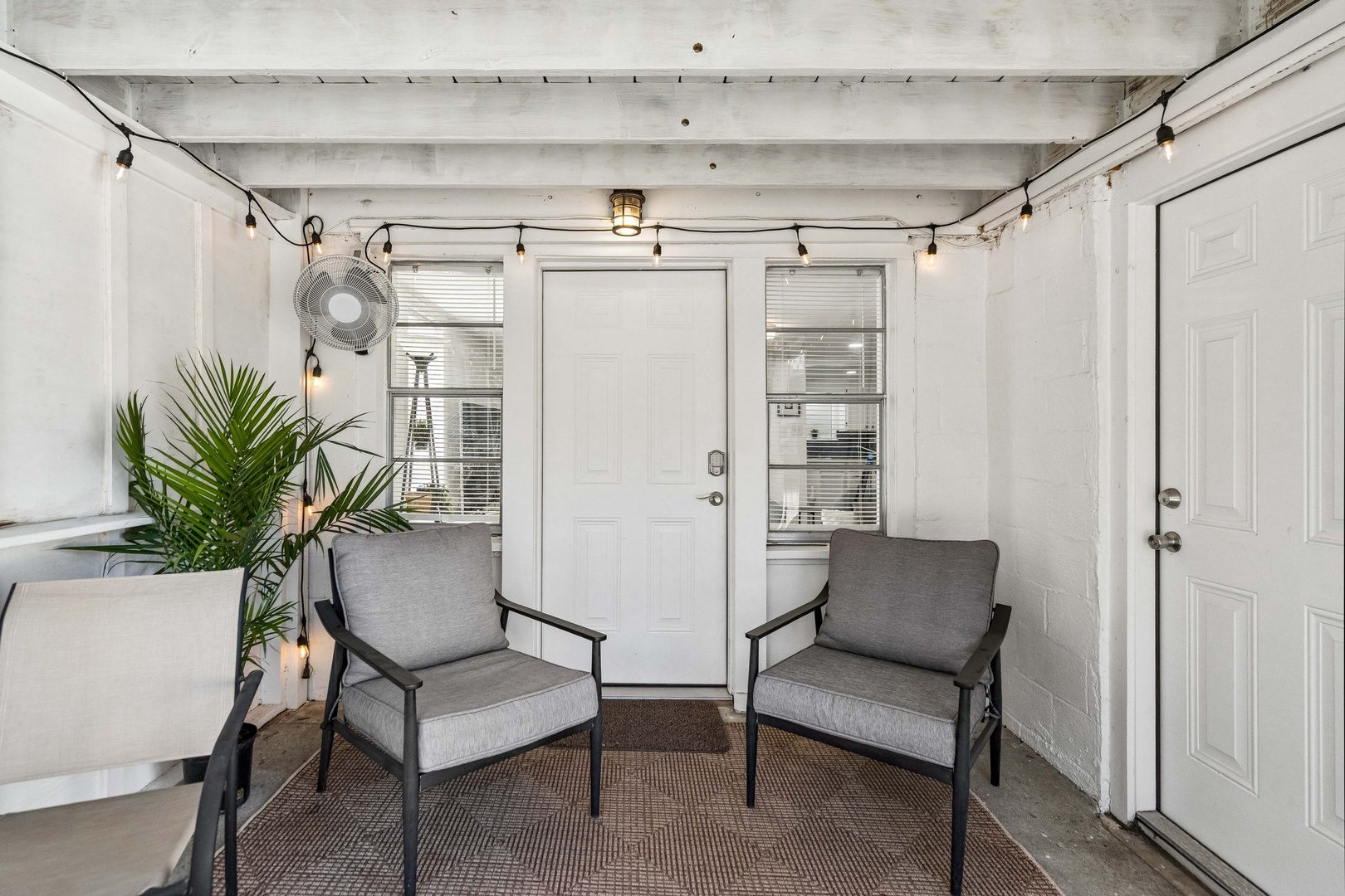 Relax in your private covered patio with modern seating, ambient string lights, and tropical plants creating the perfect retreat.