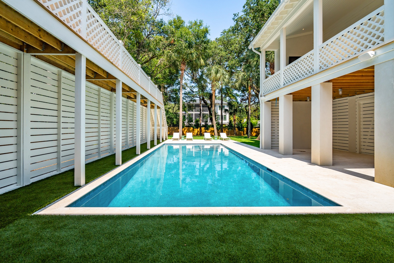 A sparkling pool stretches between elegant white buildings with lattice balconies, surrounded by lush trees and manicured lawns—your private resort oasis.