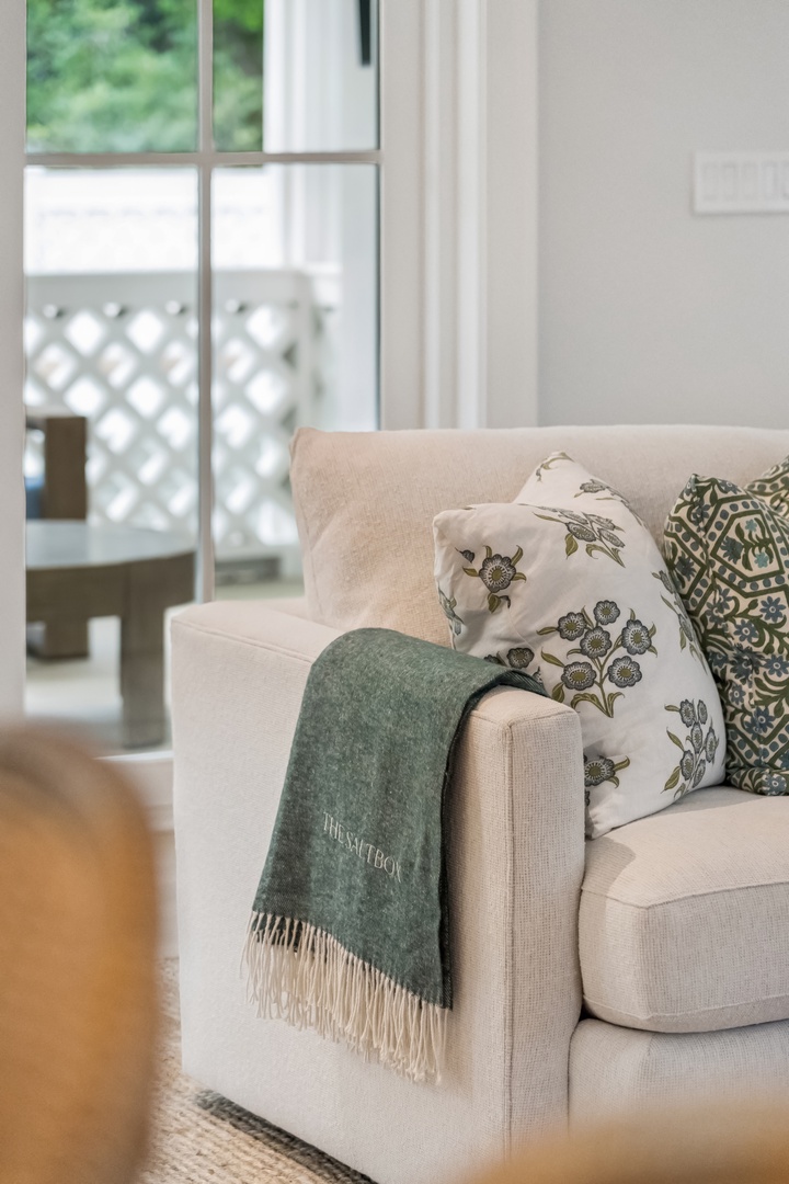 Sink into plush comfort in your living area, where soft throws and botanical-print cushions invite you to unwind by the sunlit window.