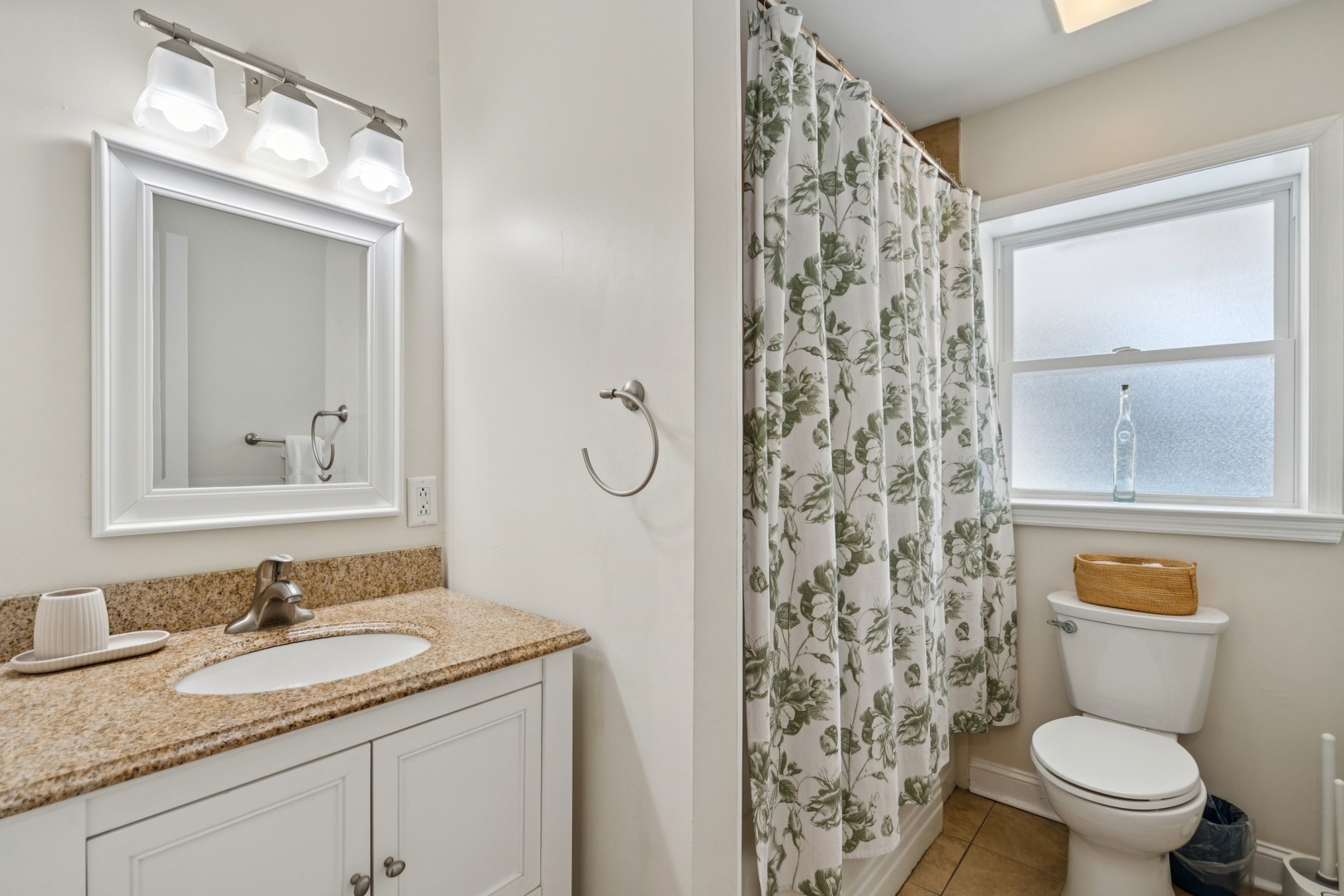 Step into your private bathroom with elegant granite countertops, charming botanical shower curtain, and crisp white fixtures that create a fresh, welcoming space for your morning routine.