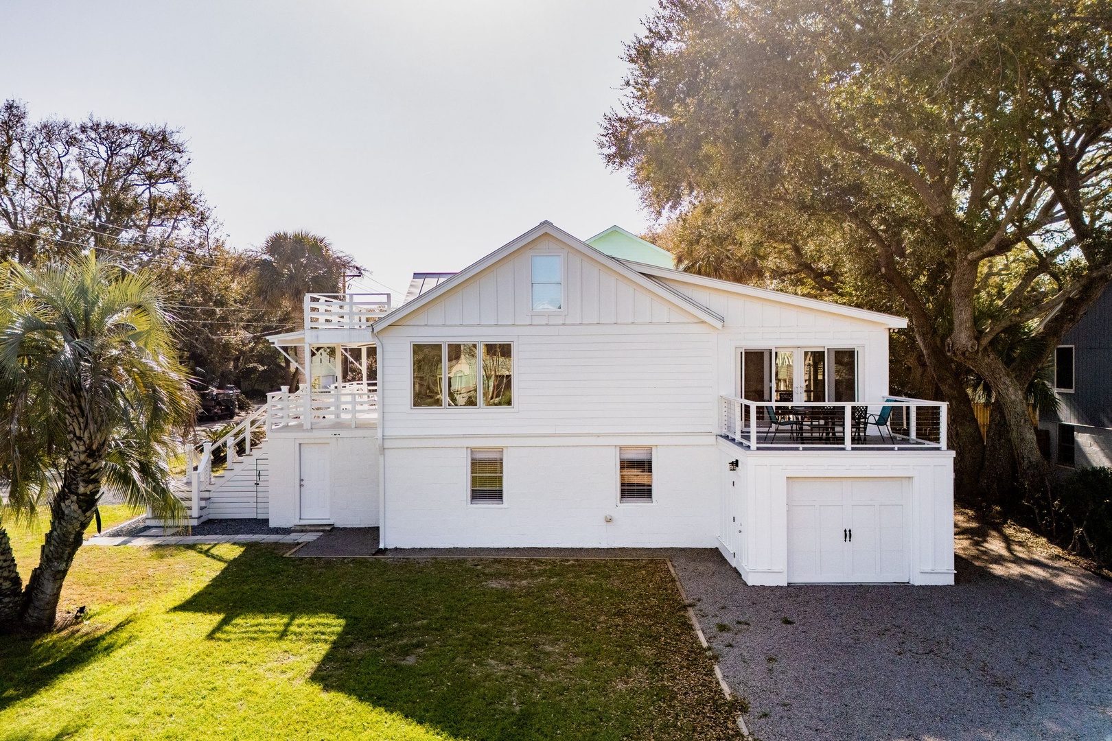 Charming coastal cottage with elevated deck surrounded by lush tropical landscaping and mature trees.