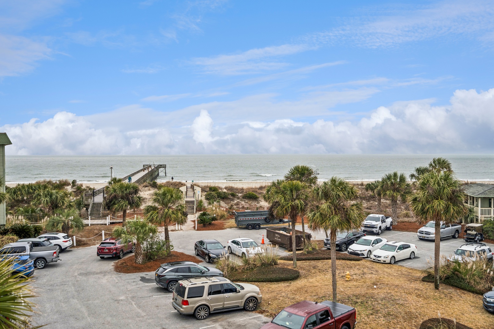 Oceanfront resort community with beach access walkway, parking facilities, and coastal palm landscapes under expansive blue skies.