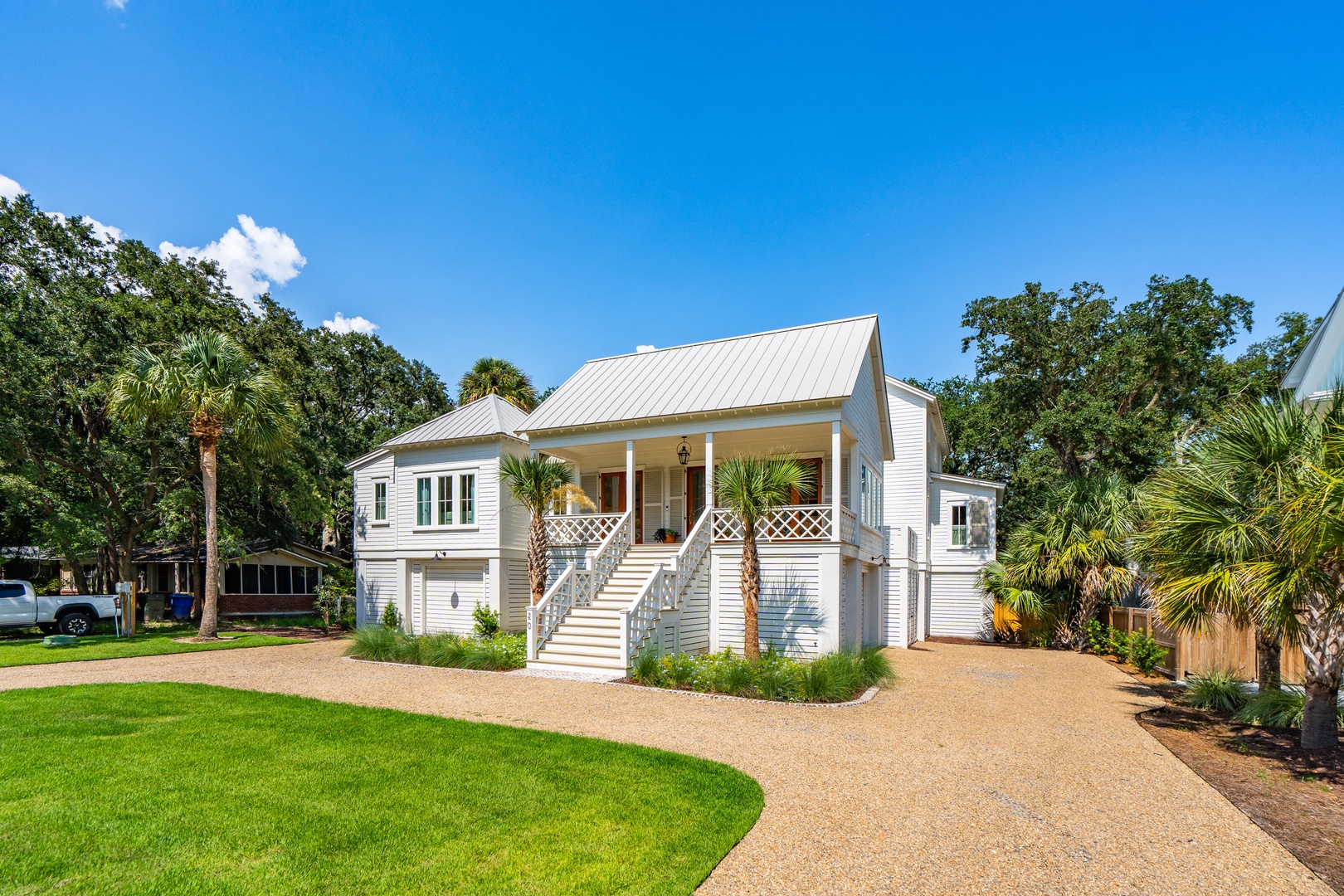 A charming coastal cottage with elevated design, surrounded by lush palms and mature trees. The property features a covered front porch and private driveway, set in a tranquil neighborhood.