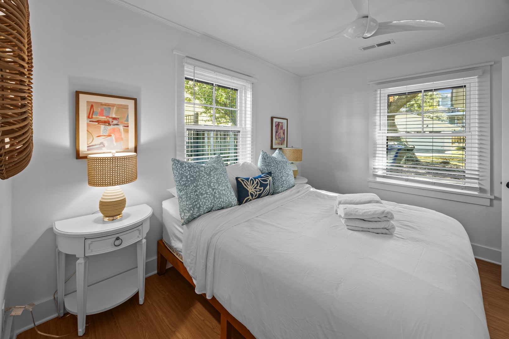 Sink into crisp white linens in this bright, airy bedroom where twin windows frame leafy views and coastal-inspired decor creates your perfect retreat.