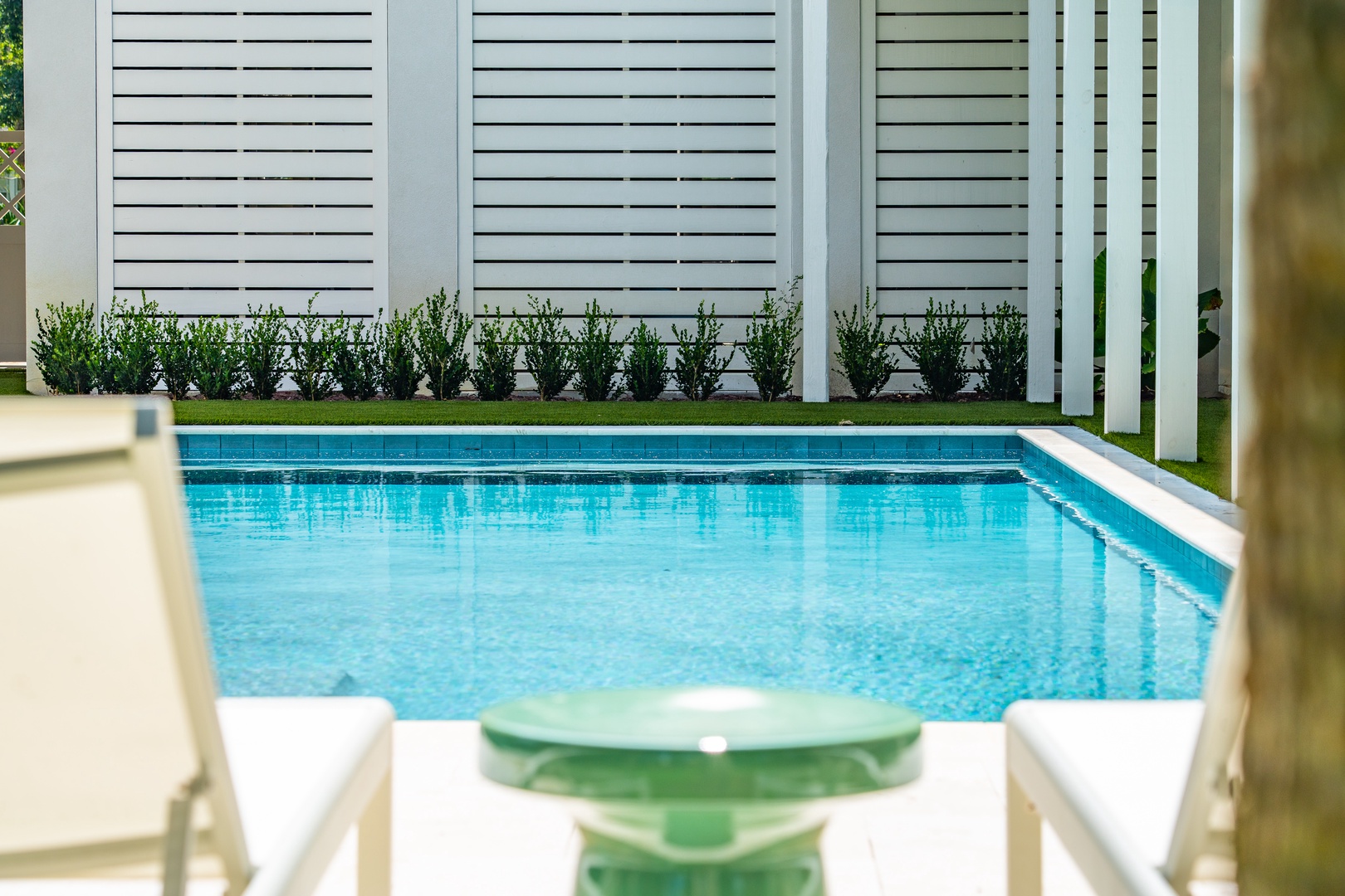 Step out to your private pool oasis, where sleek white shutters frame a pristine turquoise pool. Relax poolside with inviting seating and lush greenery—your perfect retreat for sunny days.