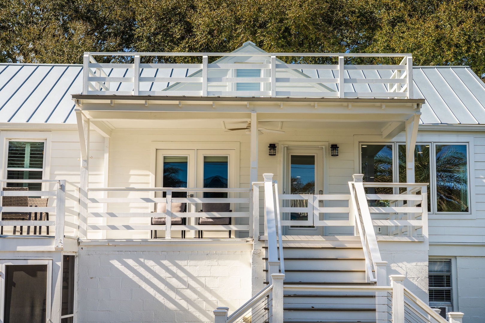Pristine white beach house featuring spacious wraparound porches and rooftop deck surrounded by mature trees.