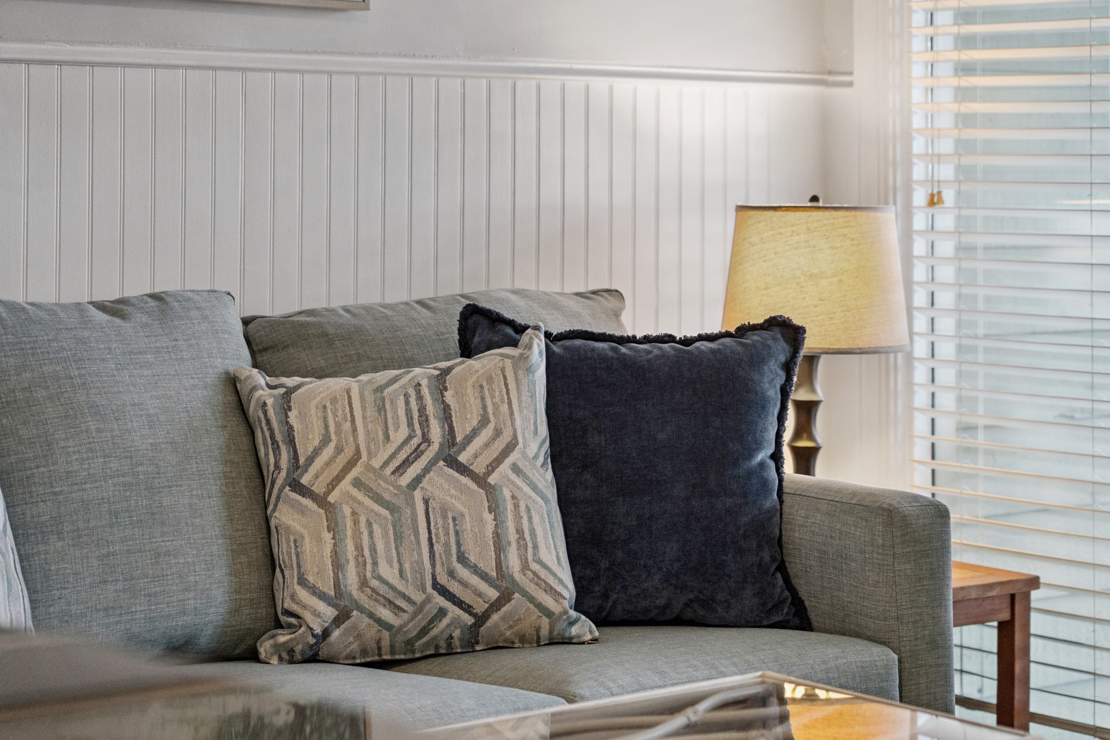 Sink into this plush sofa adorned with designer pillows, where soft textures and coastal charm create your perfect relaxation spot.