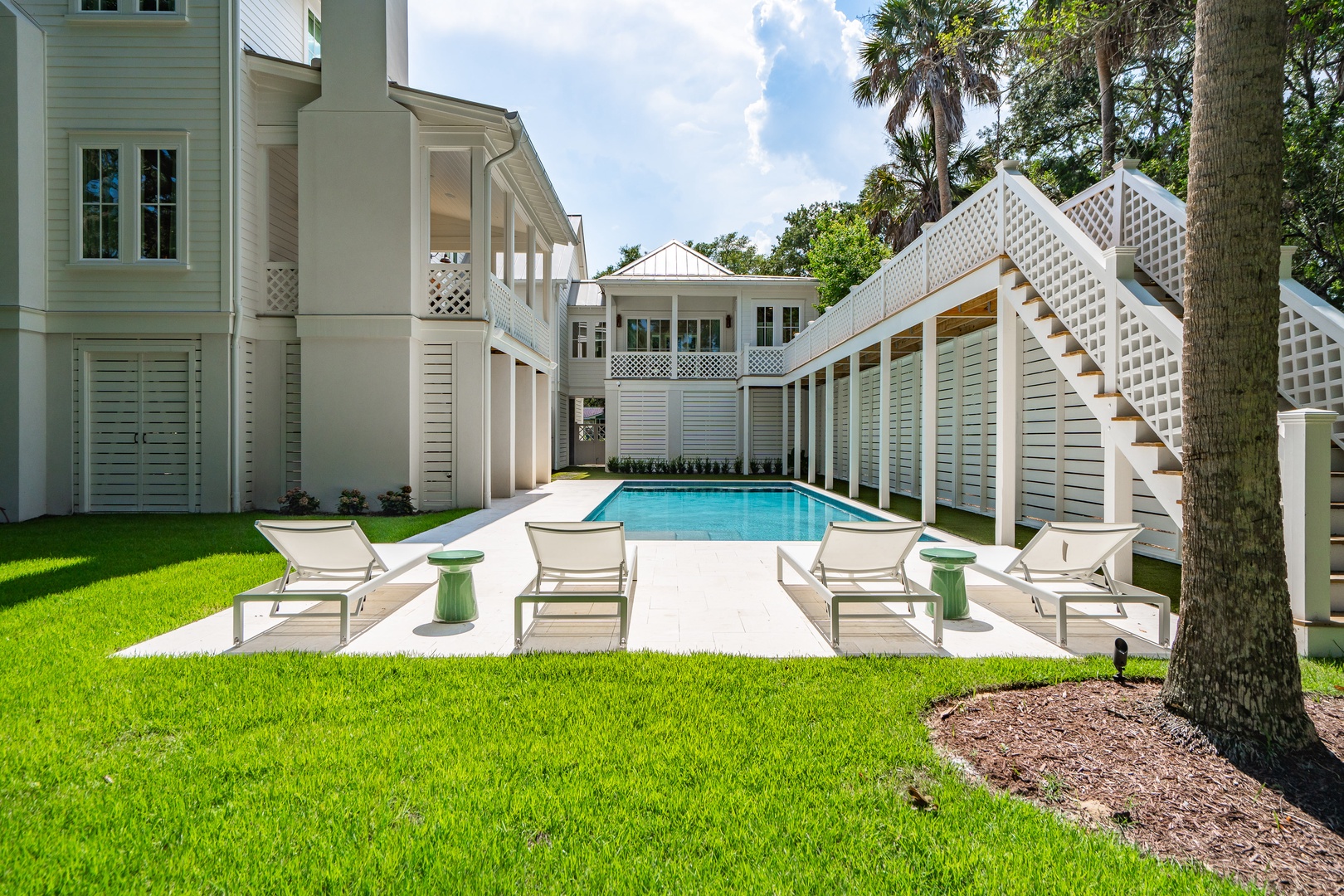 A pristine pool courtyard framed by elegant white architecture, where lush palms and manicured lawn create your private tropical retreat for sun-soaked days.