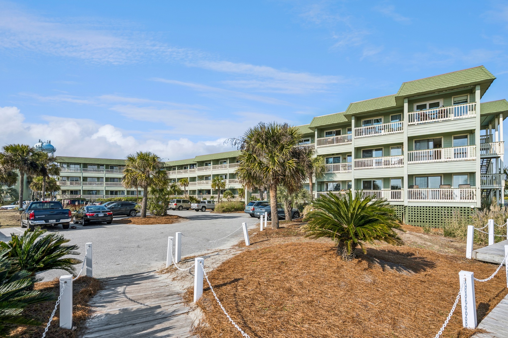 A welcoming coastal resort featuring multiple buildings with private balconies, surrounded by tropical landscaping and convenient parking.