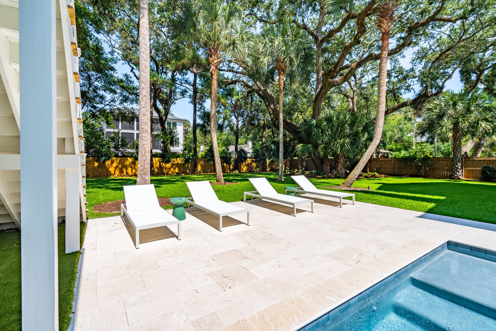 A sprawling backyard retreat framed by towering palms and lush greenery, where you can unwind on poolside loungers under the shade of mature trees.