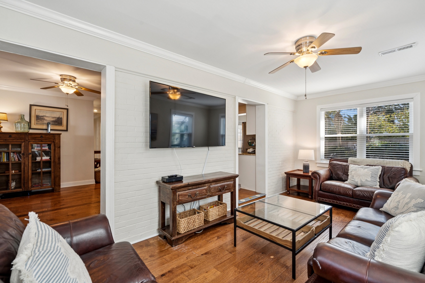 Relax in your spacious living room with plush leather seating, warm hardwood floors, and a large wall-mounted TV for cozy entertainment evenings.